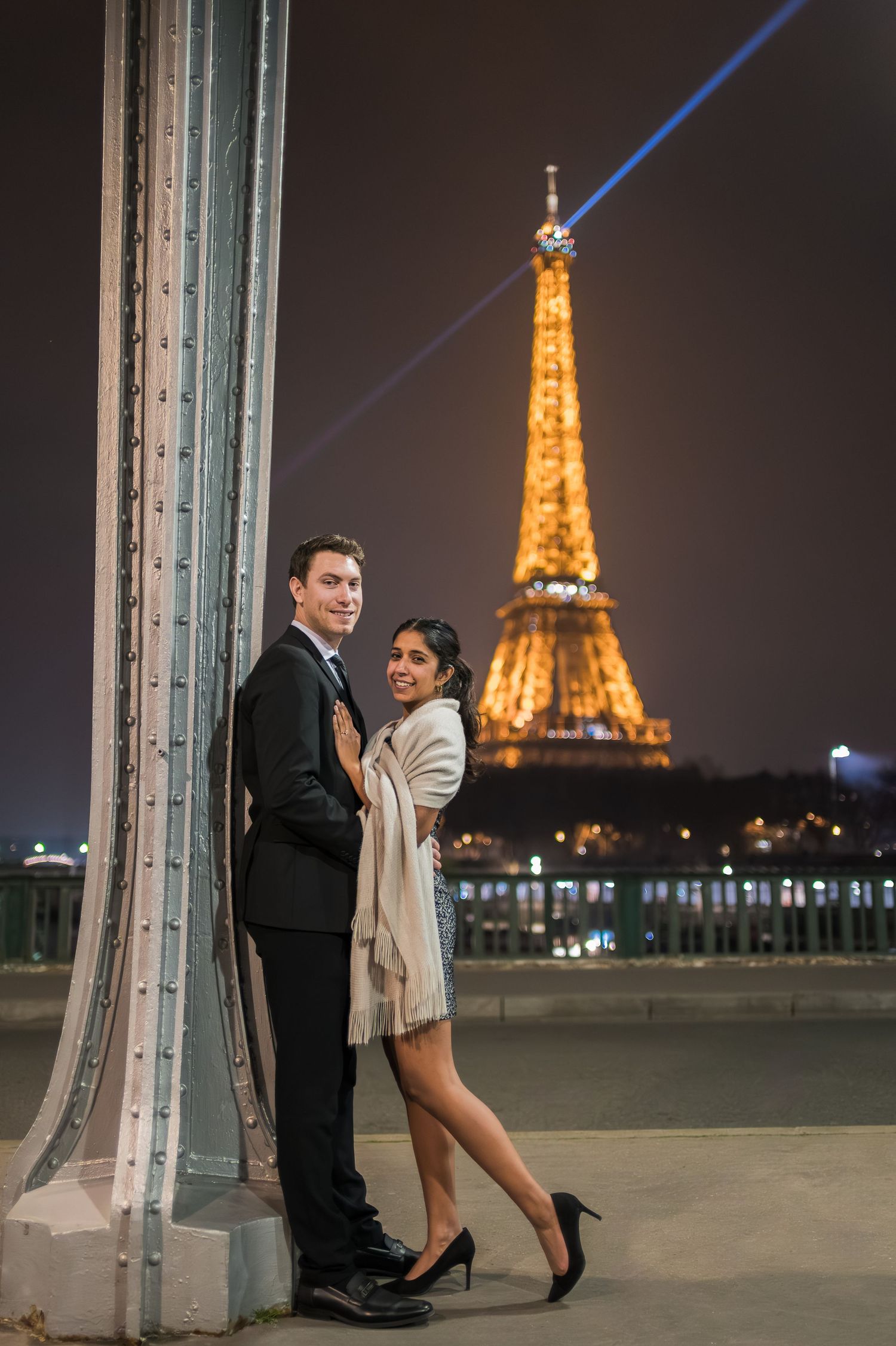 A couple poses romantically at night with the illuminated Eiffel Tower glowing in the background in Paris.