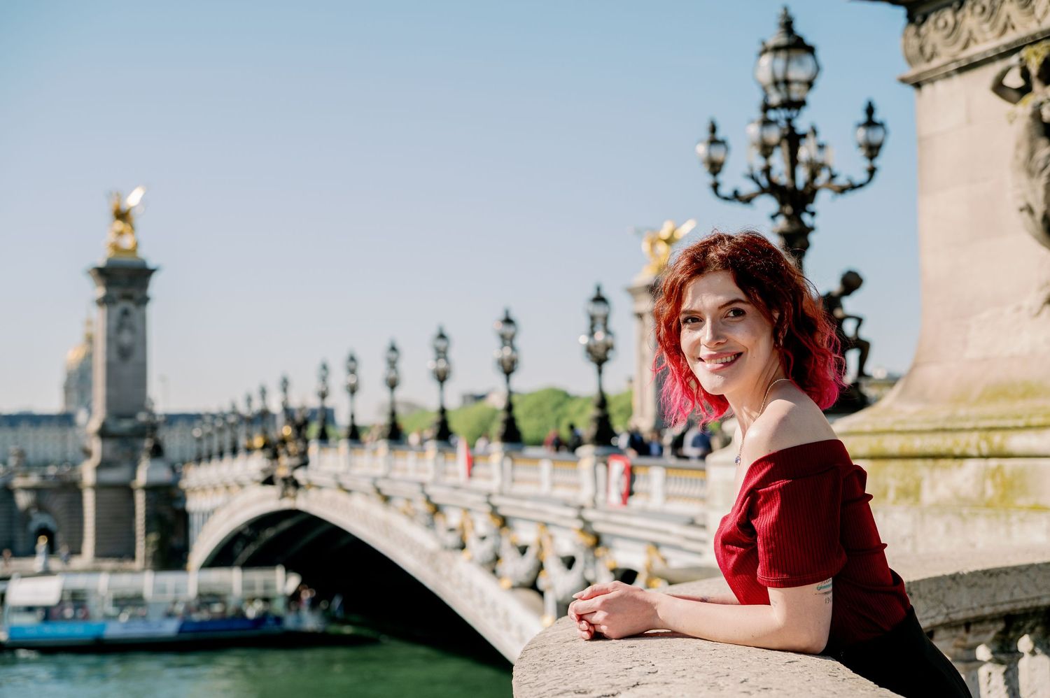 Woman in a red dress poses elegantly near ornate Parisian architecture with decorative lamp posts.