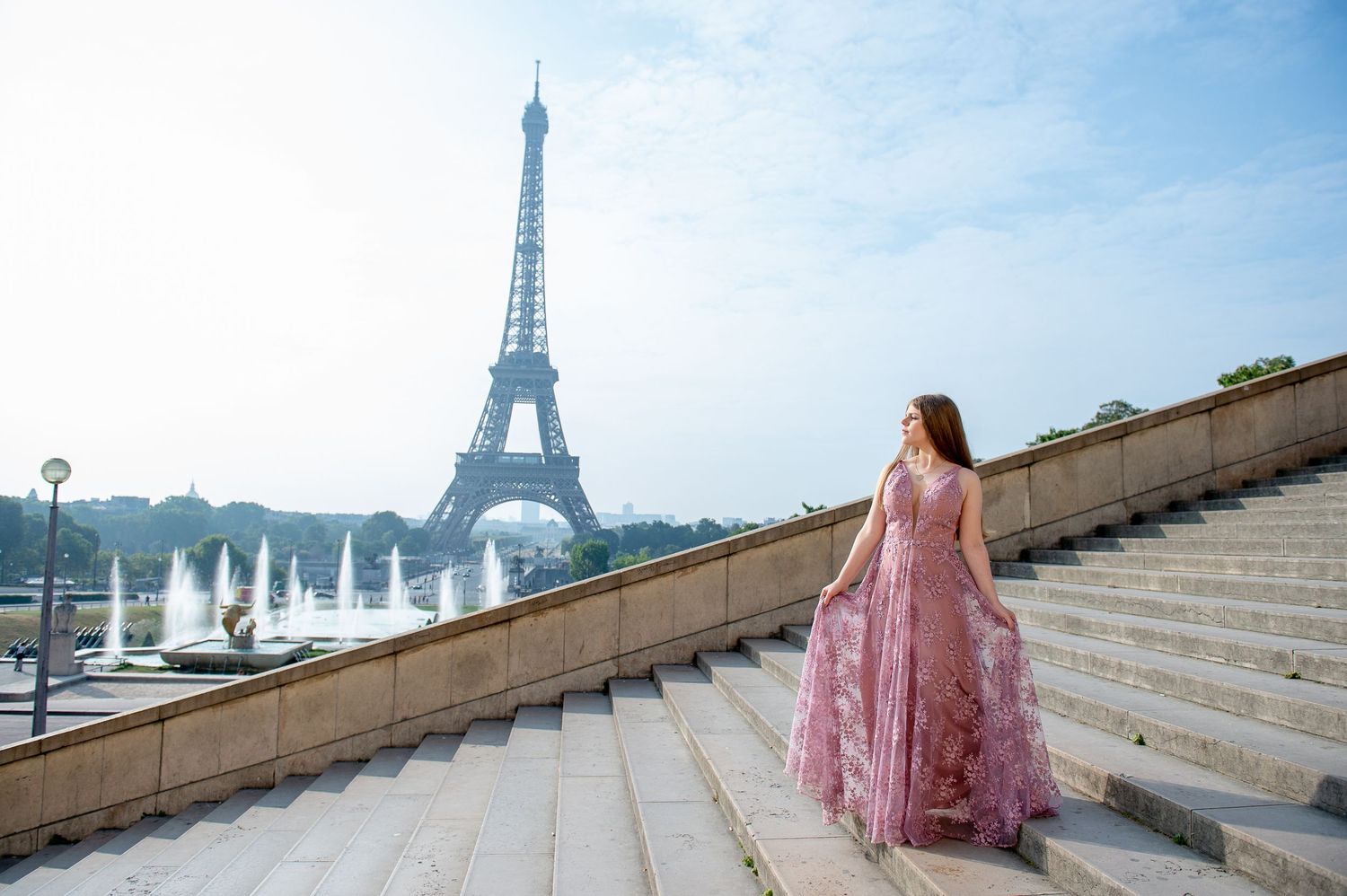 A pink flowy gown flows in the wind on the steps of Trocadero Square with the Eiffel Tower in the background.