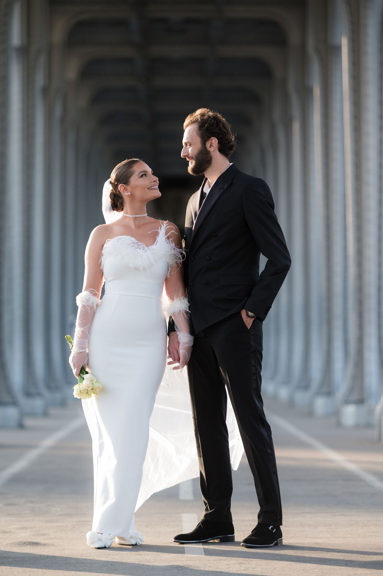 Wedding couple in formal attire standing in an elegant archway corridor with dramatic lighting and architecture.
