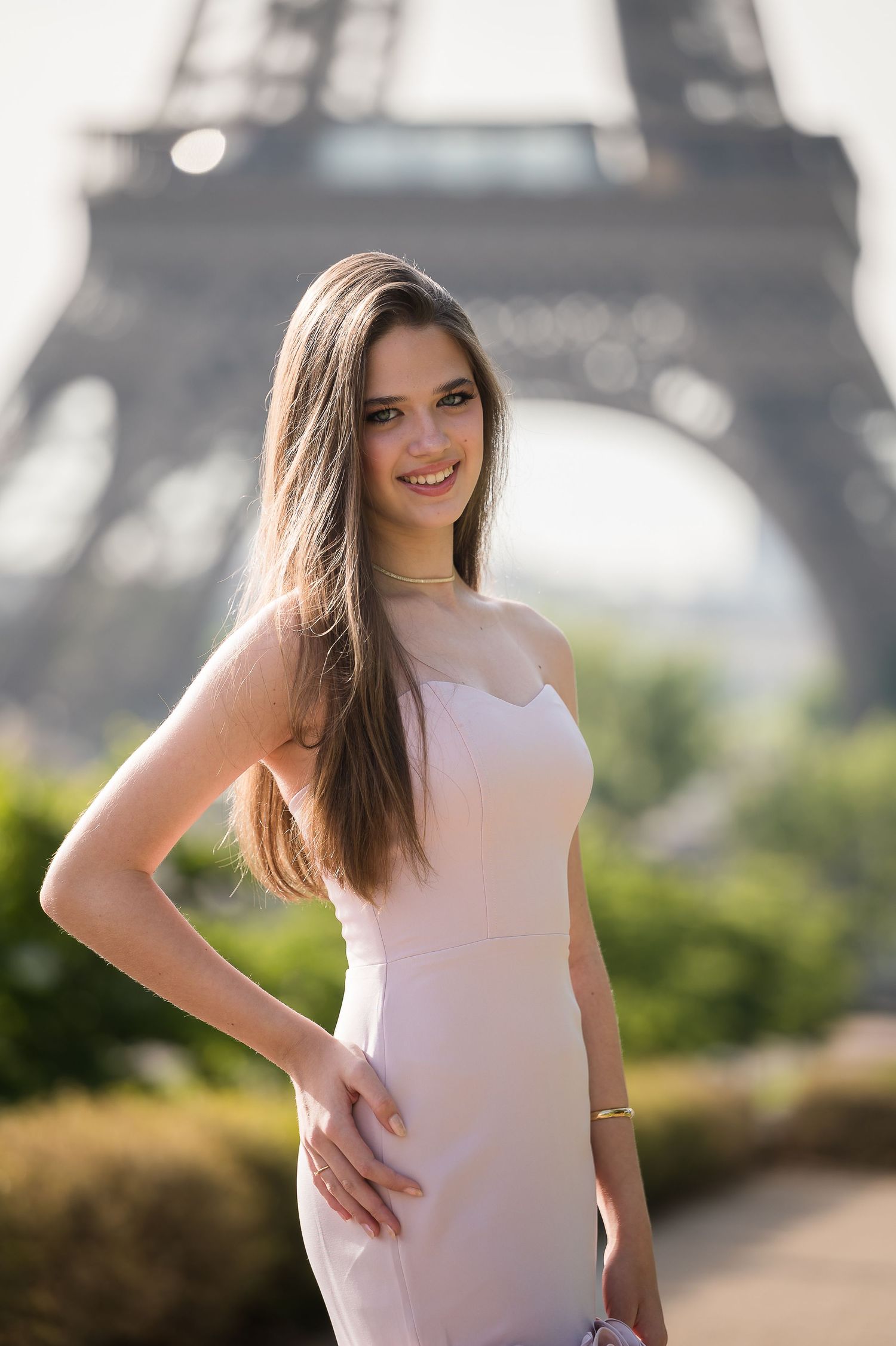Young woman in pink dress posing confidently in front of the Eiffel Tower in Paris on a sunny day.