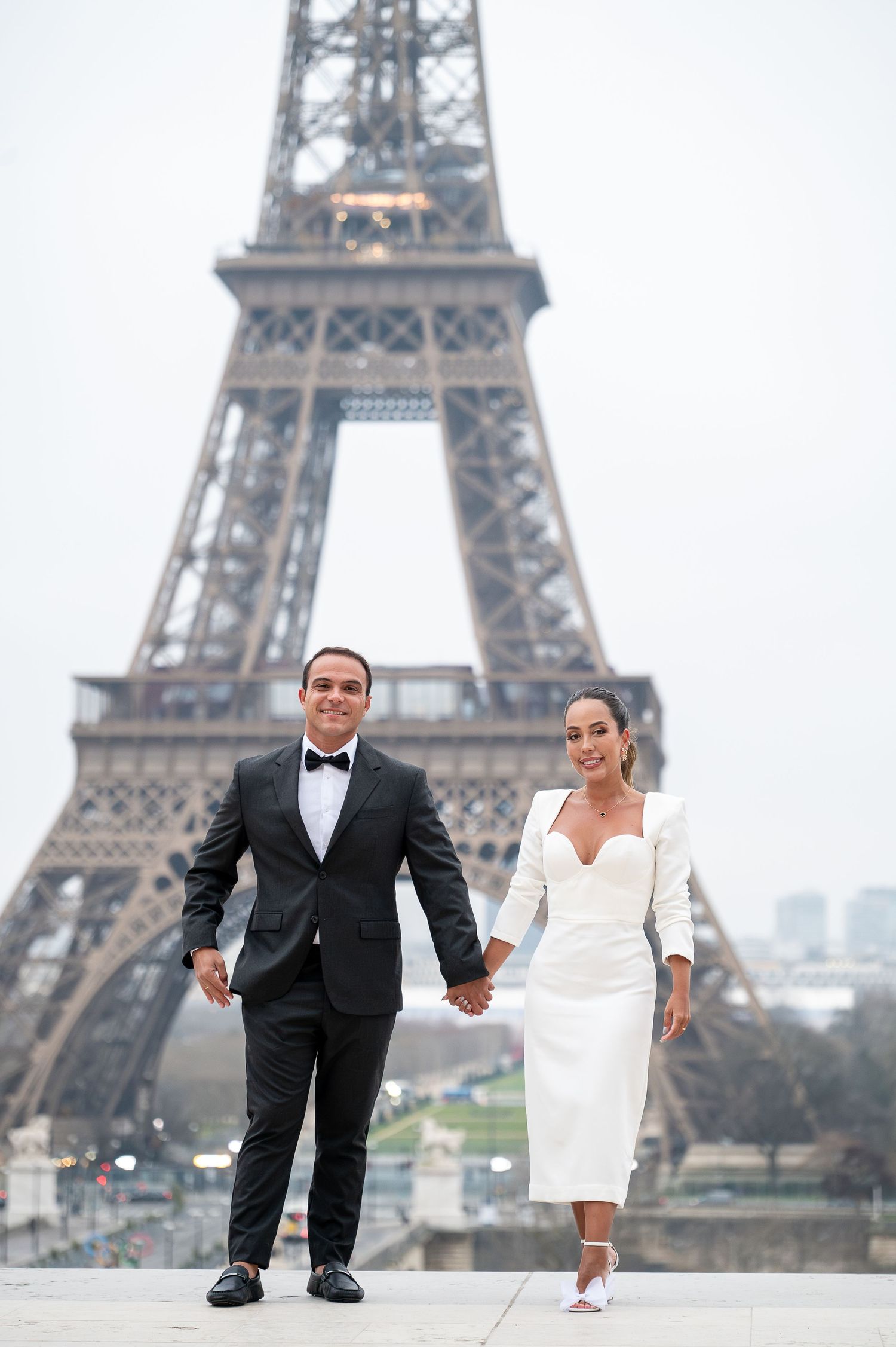 Happy couple in formal wear posing before the iconic Eiffel Tower.