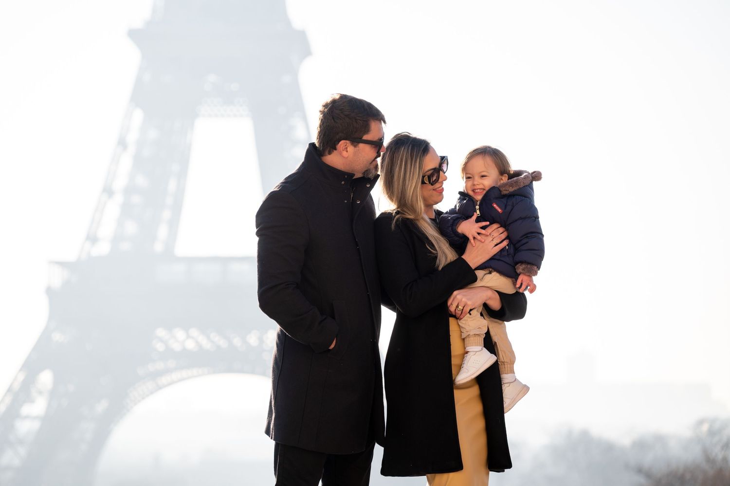 Family portrait in winter coats with misty Eiffel Tower silhouette in background.