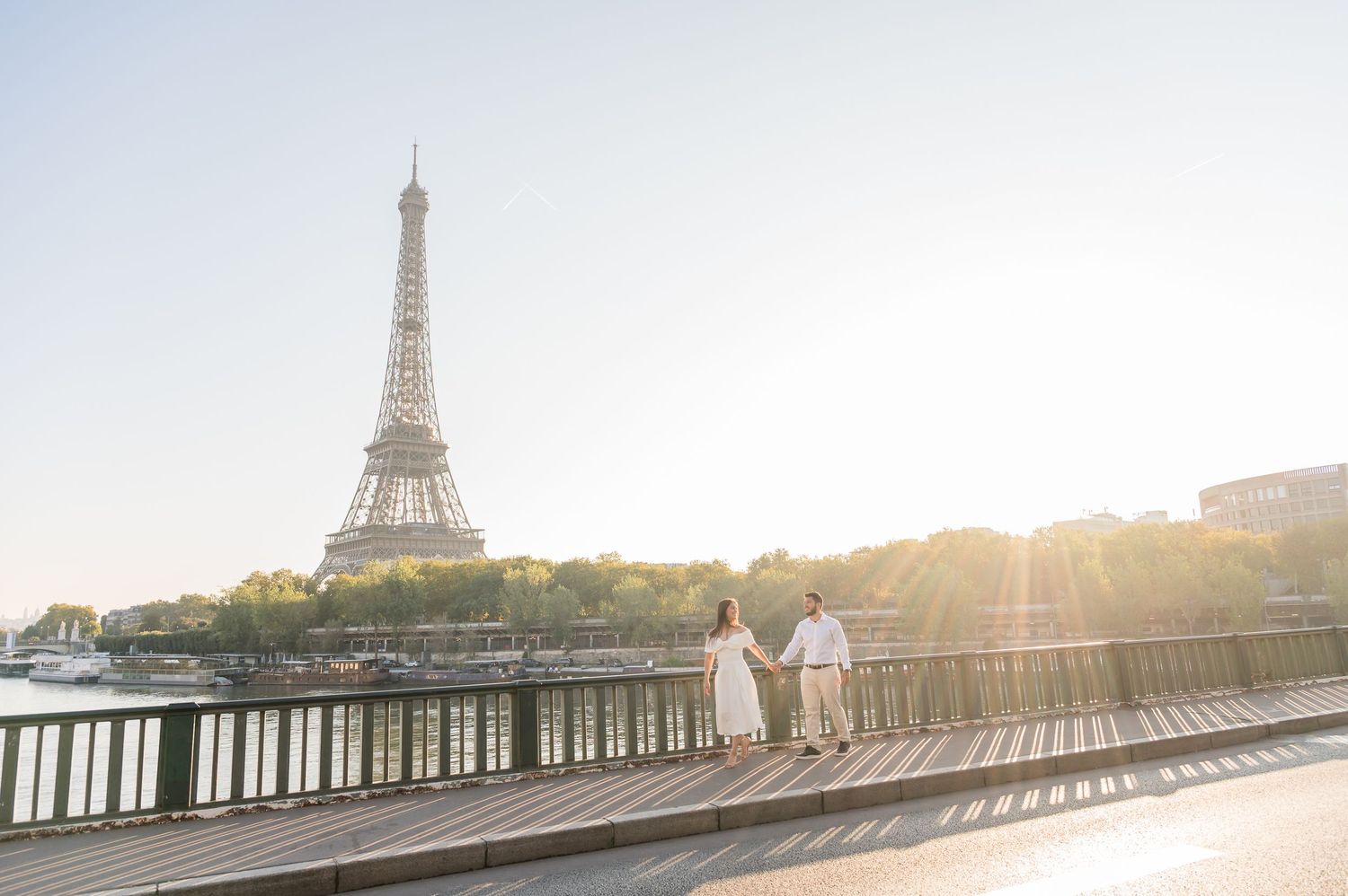 Panoramic view of the Eiffel Tower and Seine River in Paris during golden sunset with sun flare through trees.