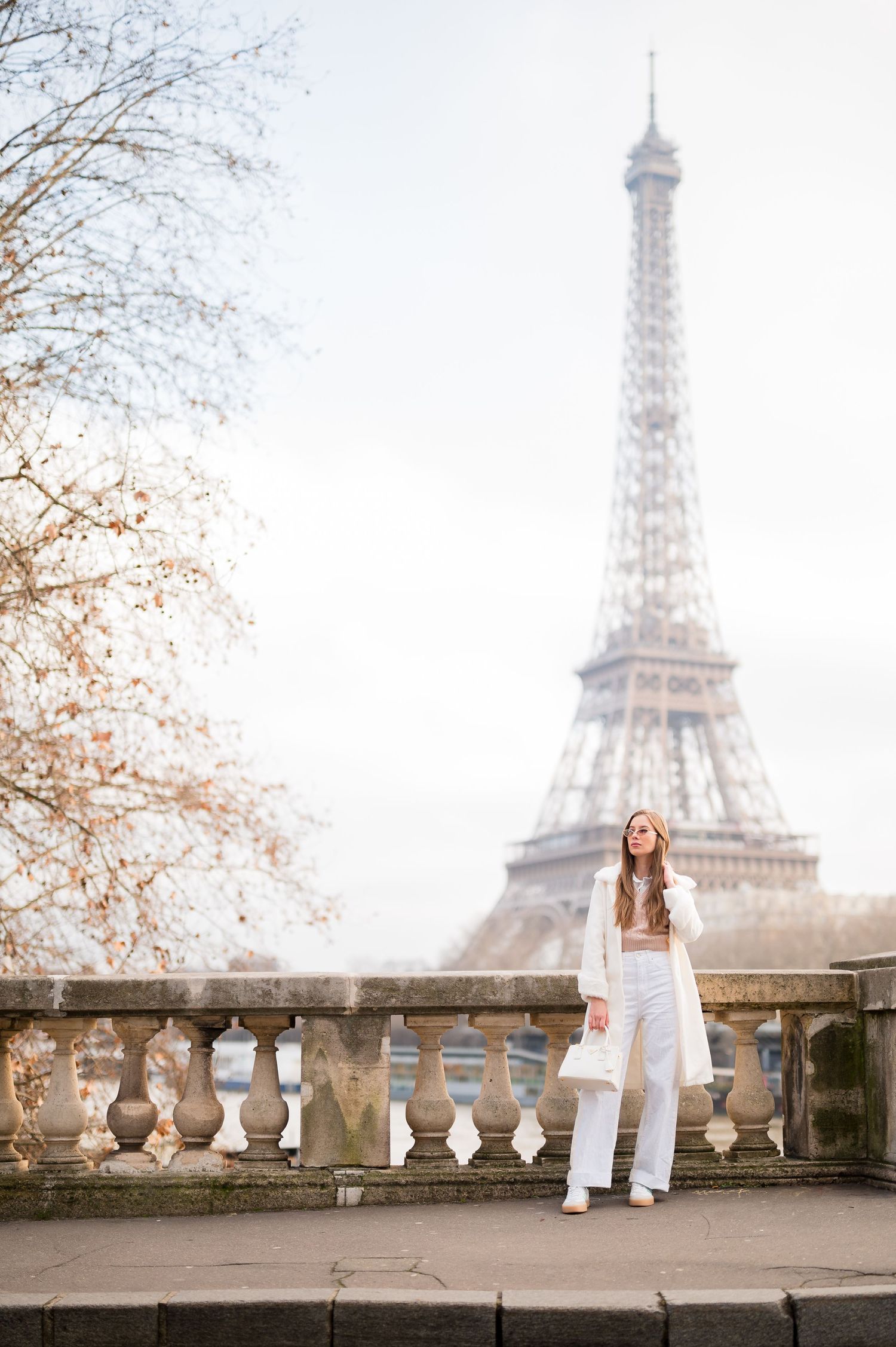 Person in white outfit standing on balcony with misty Eiffel Tower in background.