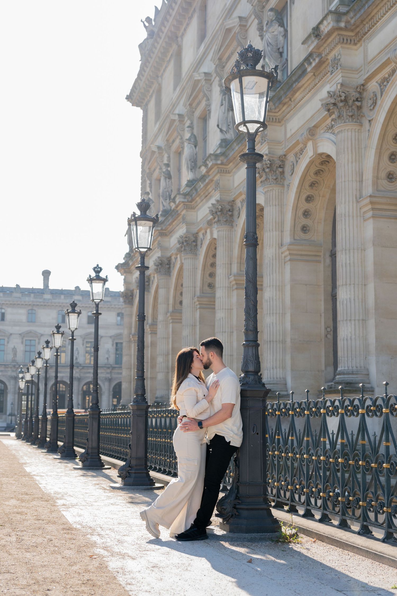 A tender moment between a couple by vintage lampposts along an ornate Parisian building.