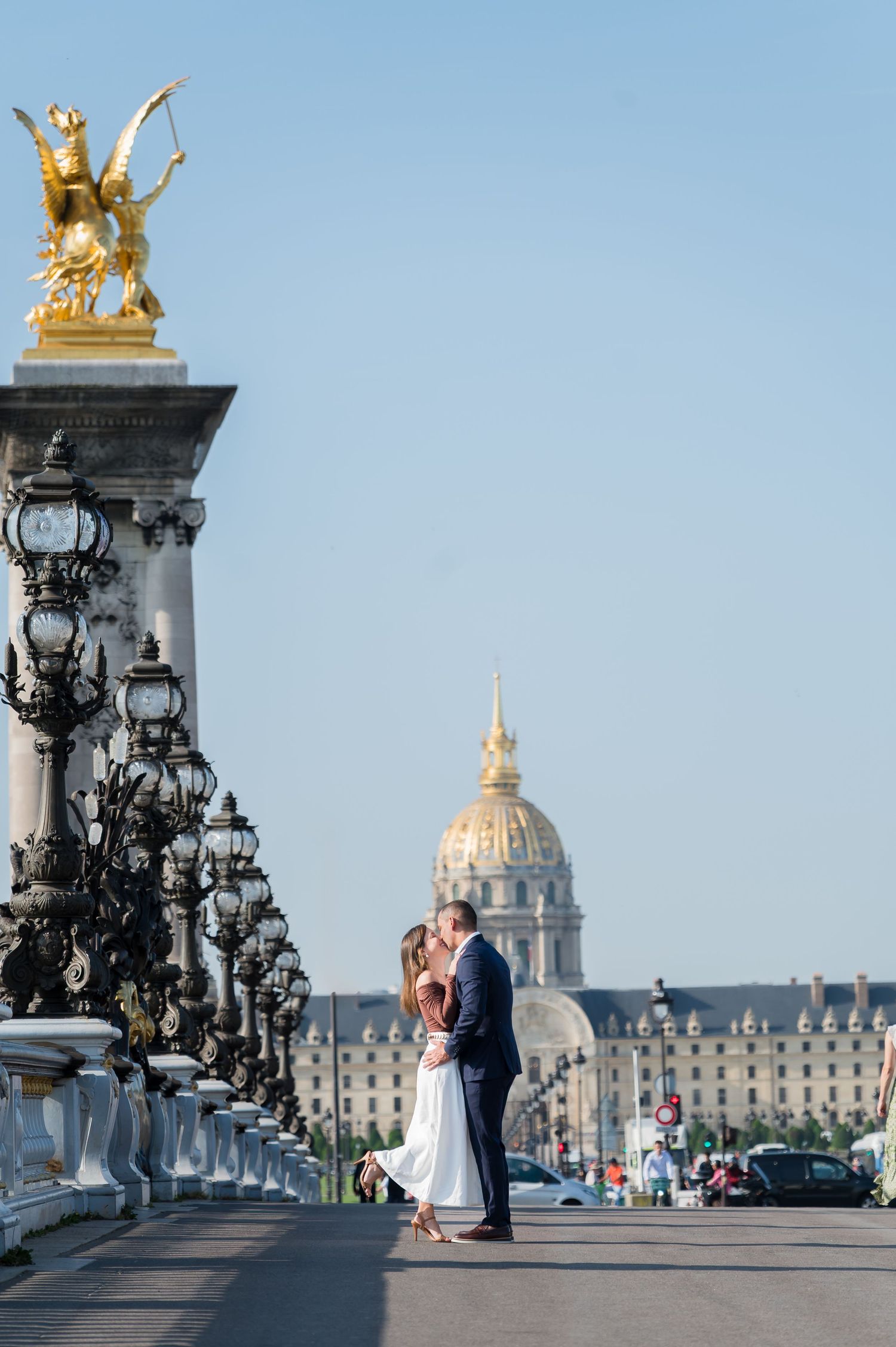 Romantic couple dancing on the historic Pont Alexandre III bridge in Paris with the golden statues and Invalides dome.