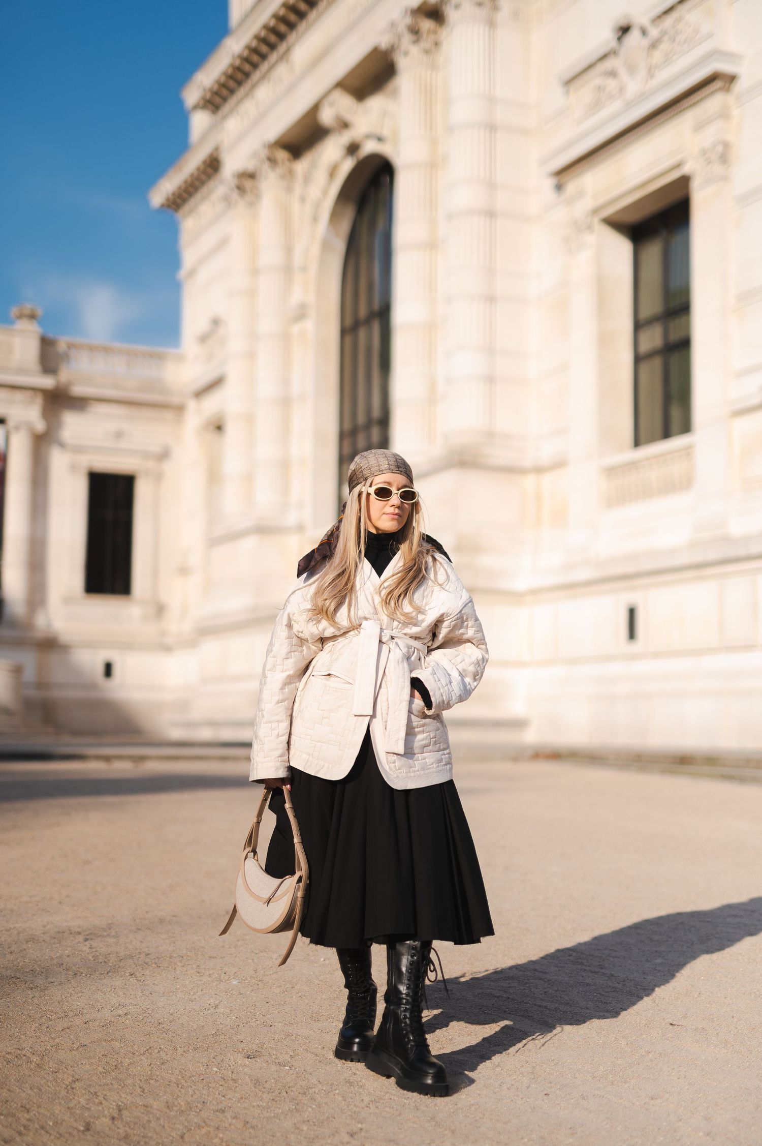Fashionable winter street style with cream jacket, black skirt and boots against classical architecture backdrop.