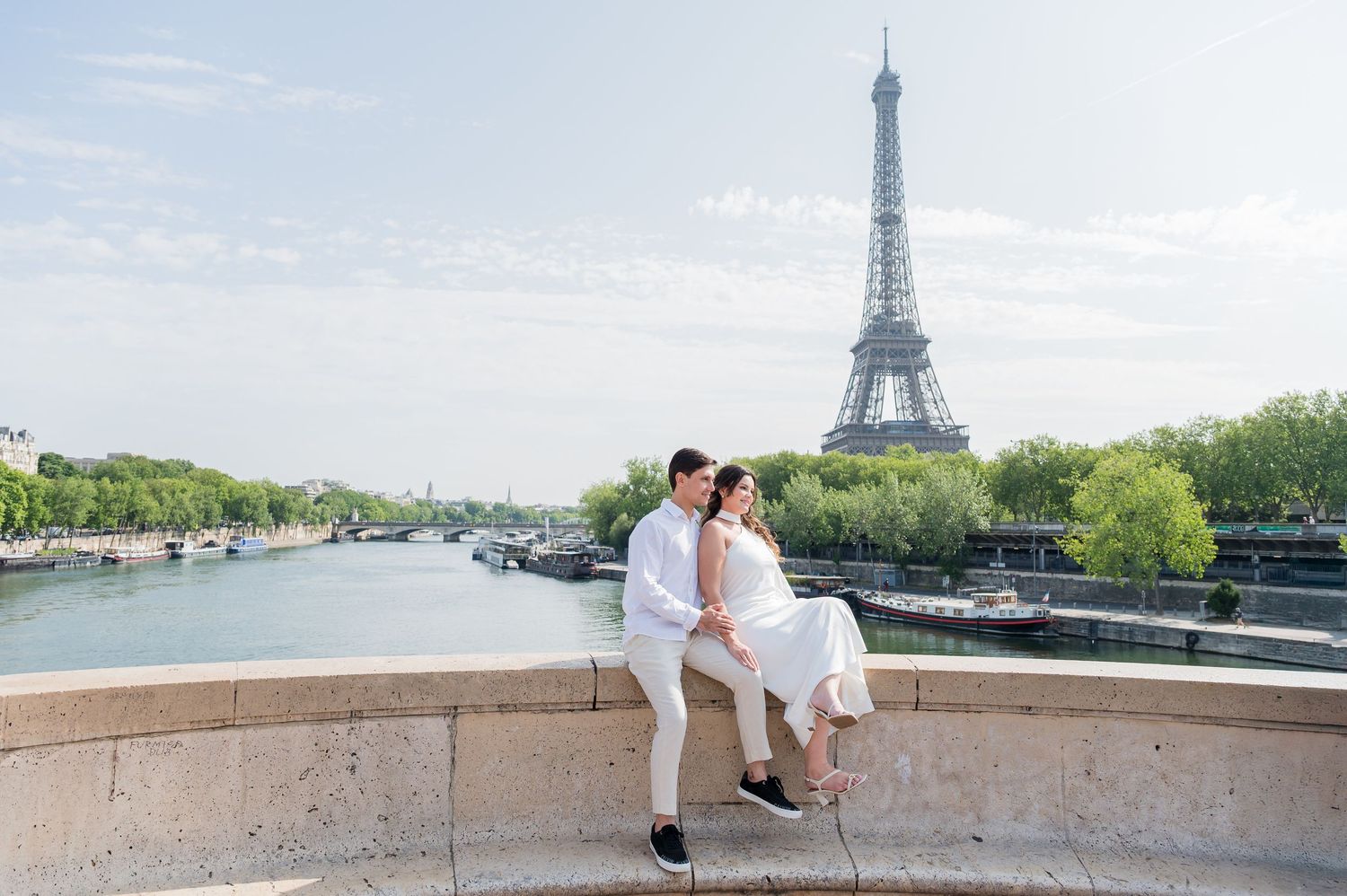Romantic couple in white taking photos with the iconic Eiffel Tower in Paris against a bright summer sky.