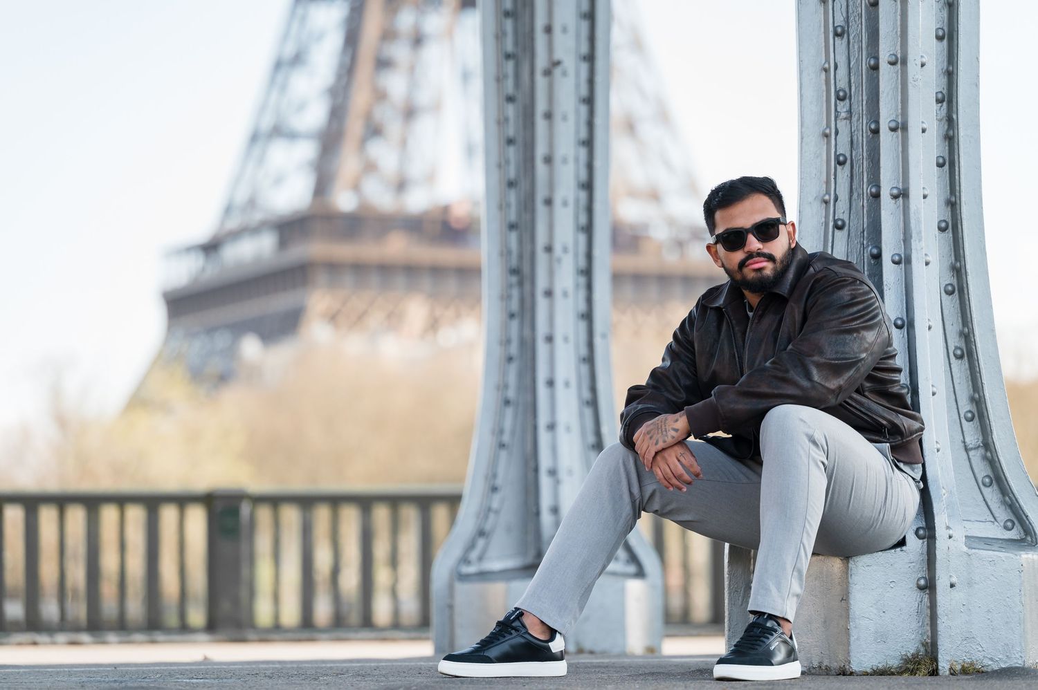 Man in sunglasses posing on a bridge with the Eiffel Tower in Paris, France in the background.