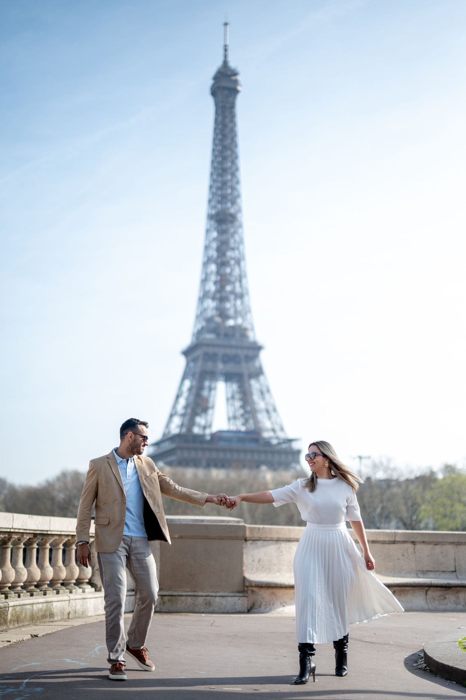 A couple dances playfully on a Parisian bridge with the Eiffel Tower in the background.