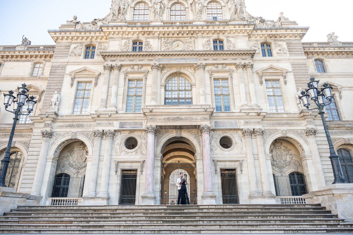 A symmetrical shot of a historic French building with a couple centered in its grand entrance.