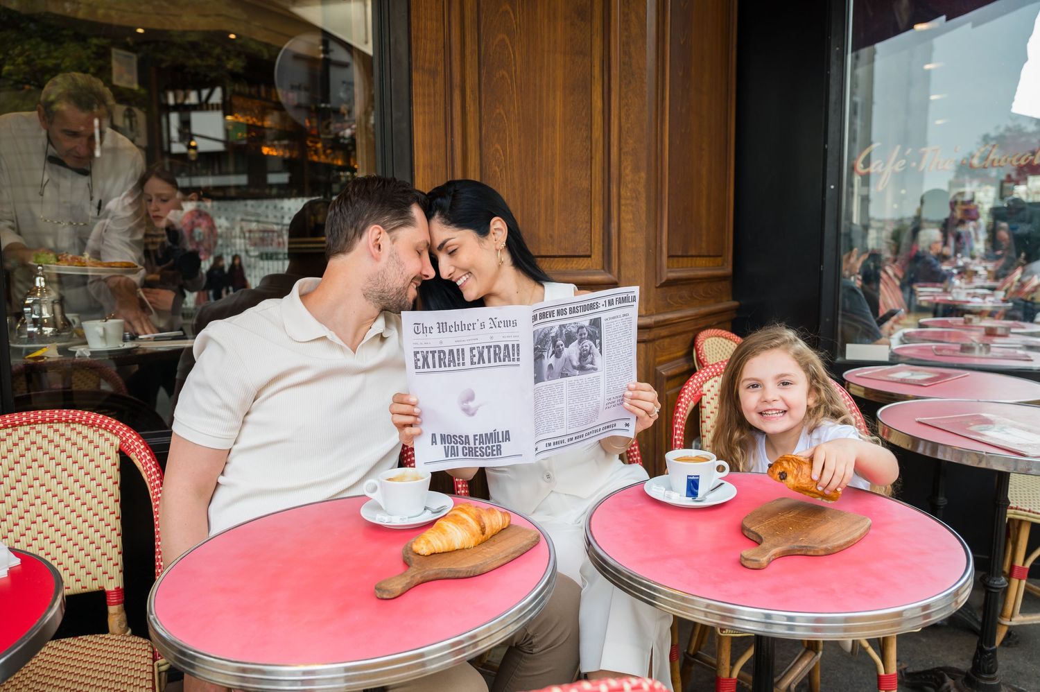 Diners enjoy coffee and pastries at outdoor cafe tables with pink tops along a Parisian sidewalk.