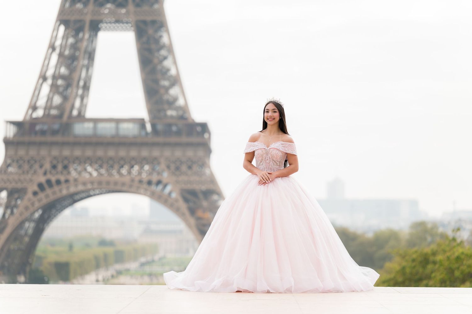 A person in a pink ballgown poses elegantly in front of the iconic Eiffel Tower in Paris.