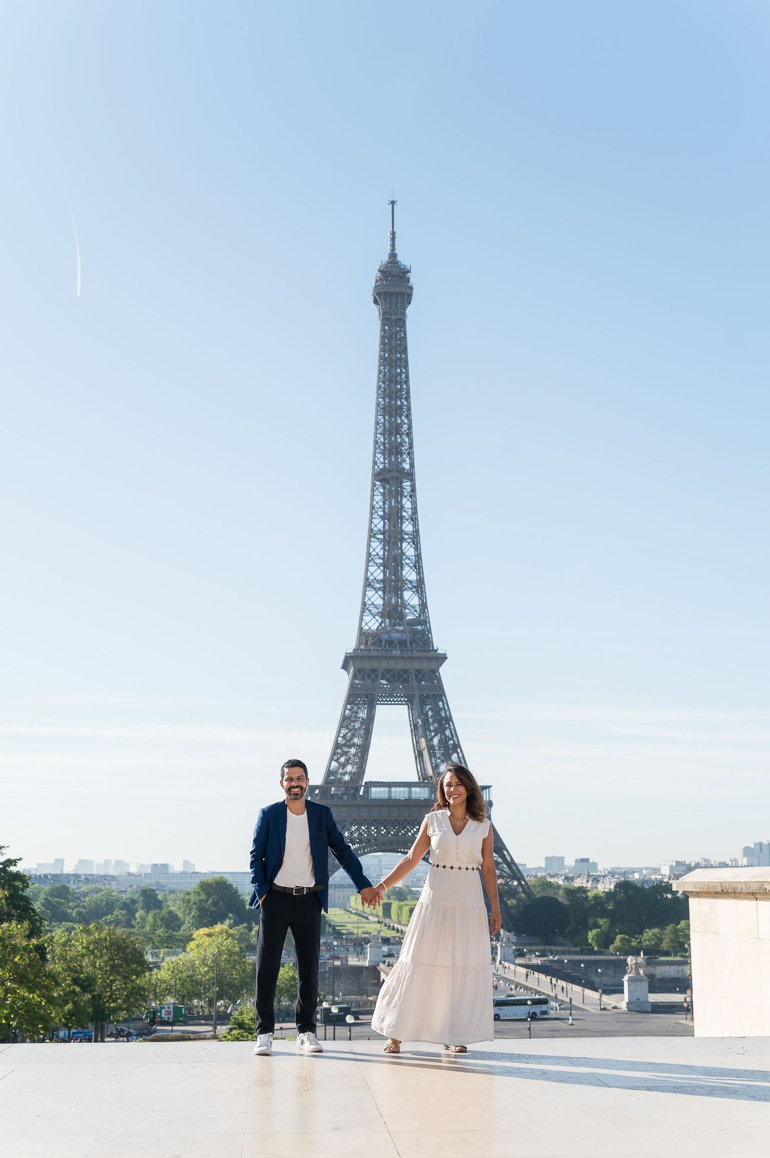Couple holding hands in front of the Eiffel Tower in Paris on a sunny day.