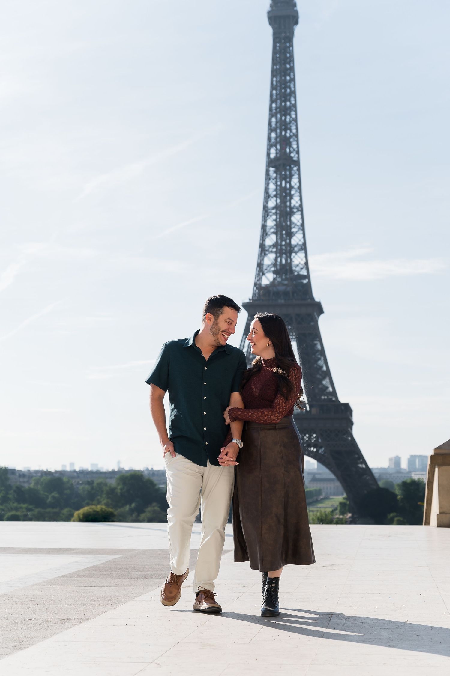 Couple holding hands and smiling while walking in front of the Eiffel Tower in Paris, France.