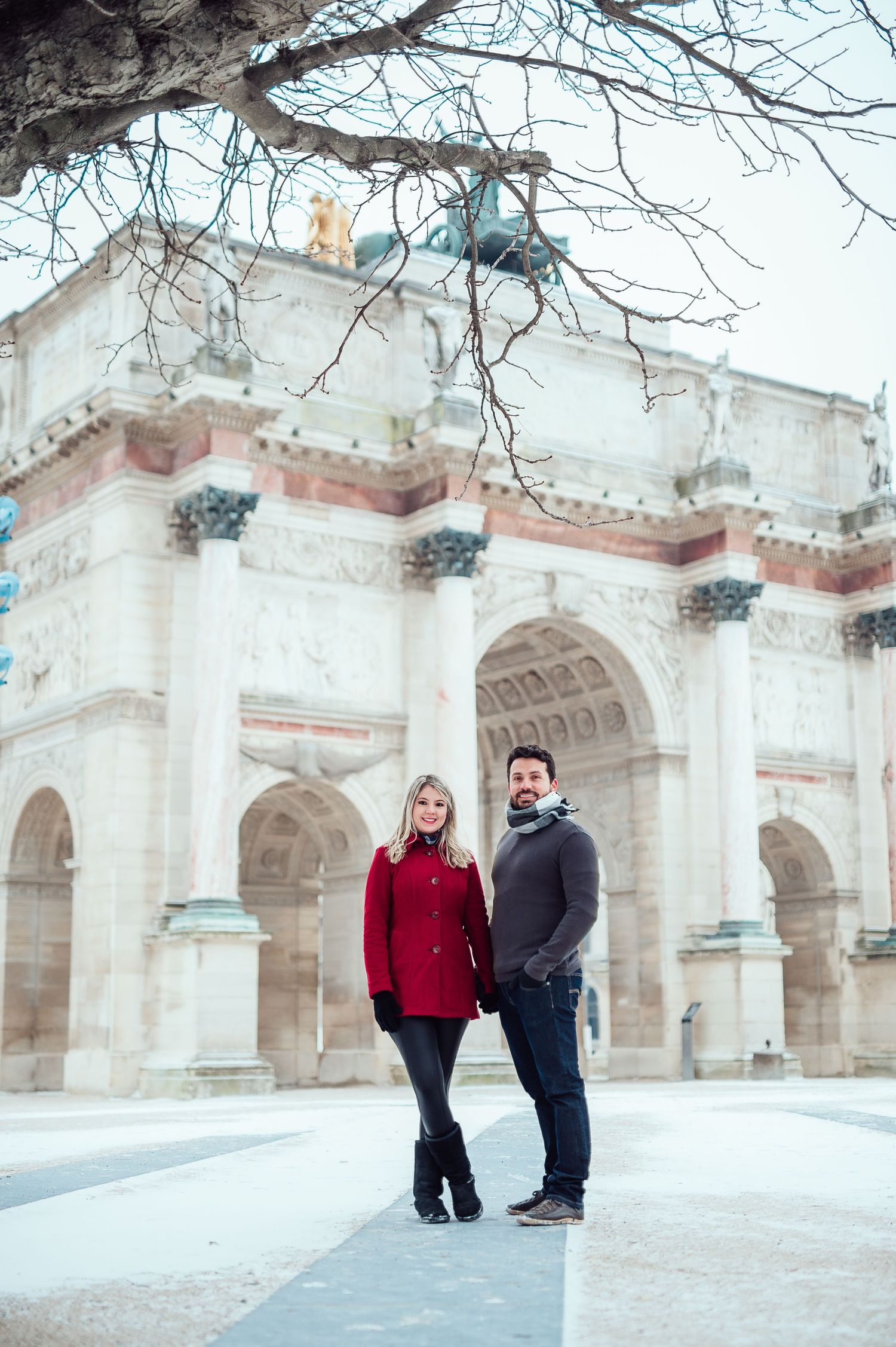 Two people stand together in warm winter clothing in front of ornate white stone archways and historic architecture.