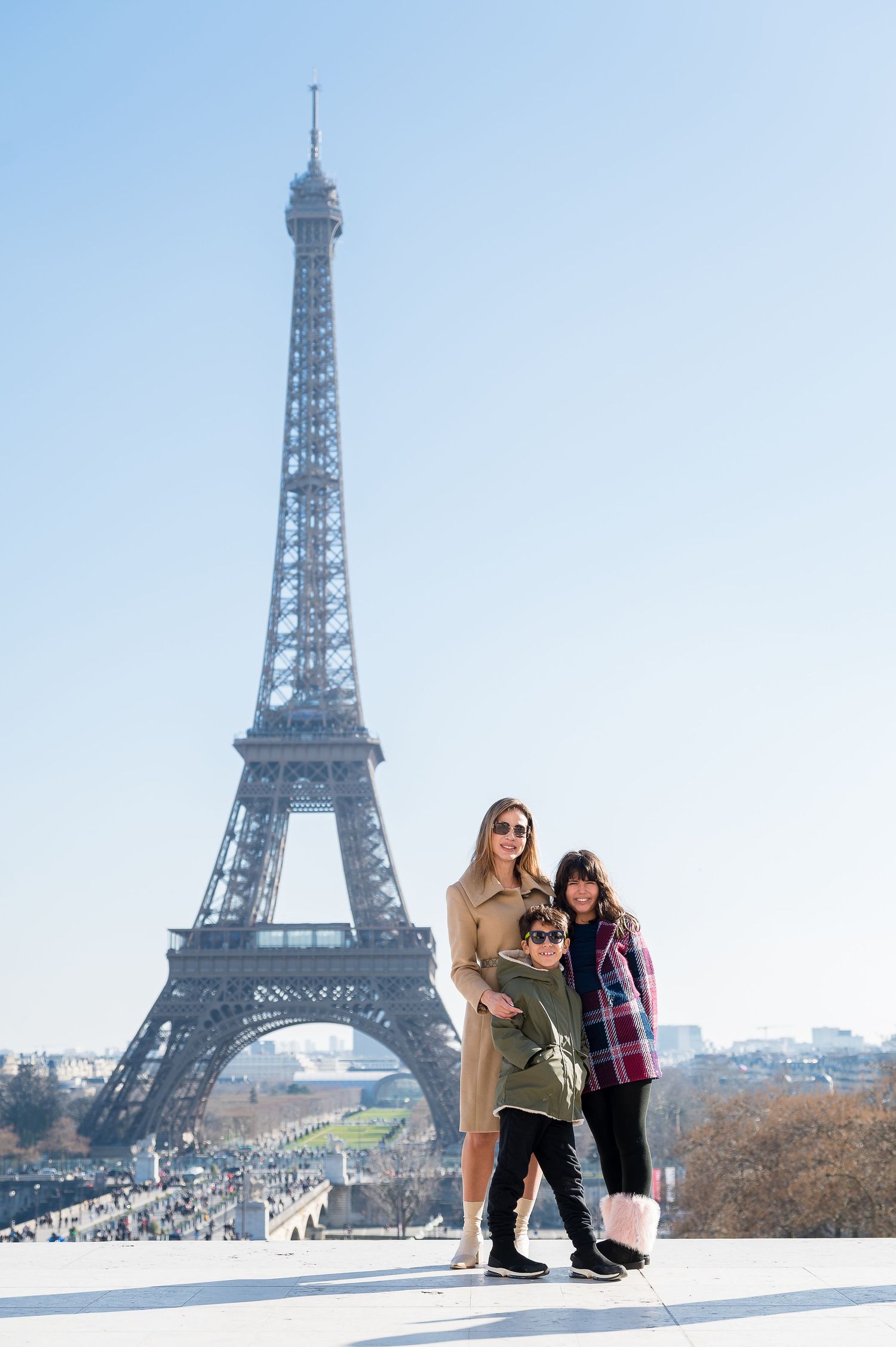 Three people stand together with the majestic Eiffel Tower framing the scene on a bright Paris day.