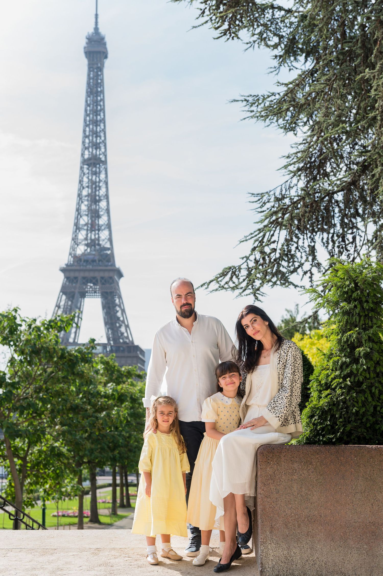 A family poses in front of the iconic Eiffel Tower in Paris on a bright summer day.