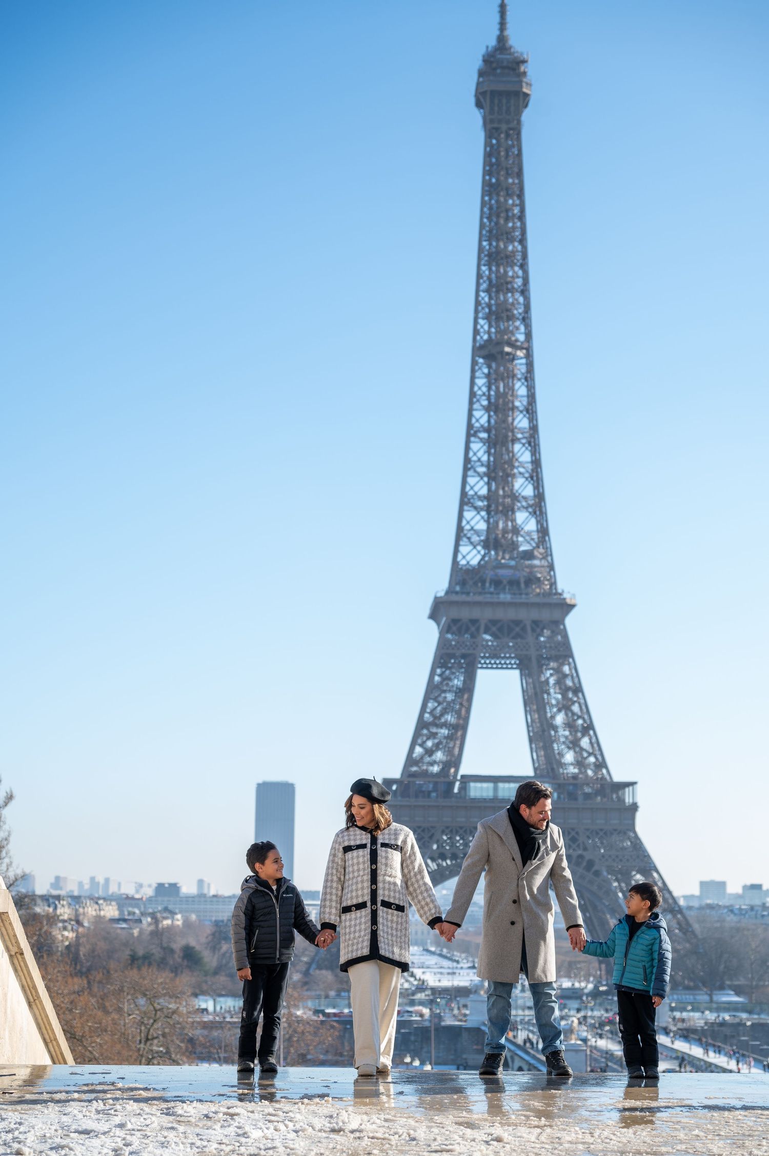A family enjoys a playful moment together on a winter day with the Eiffel Tower as their backdrop in Paris.