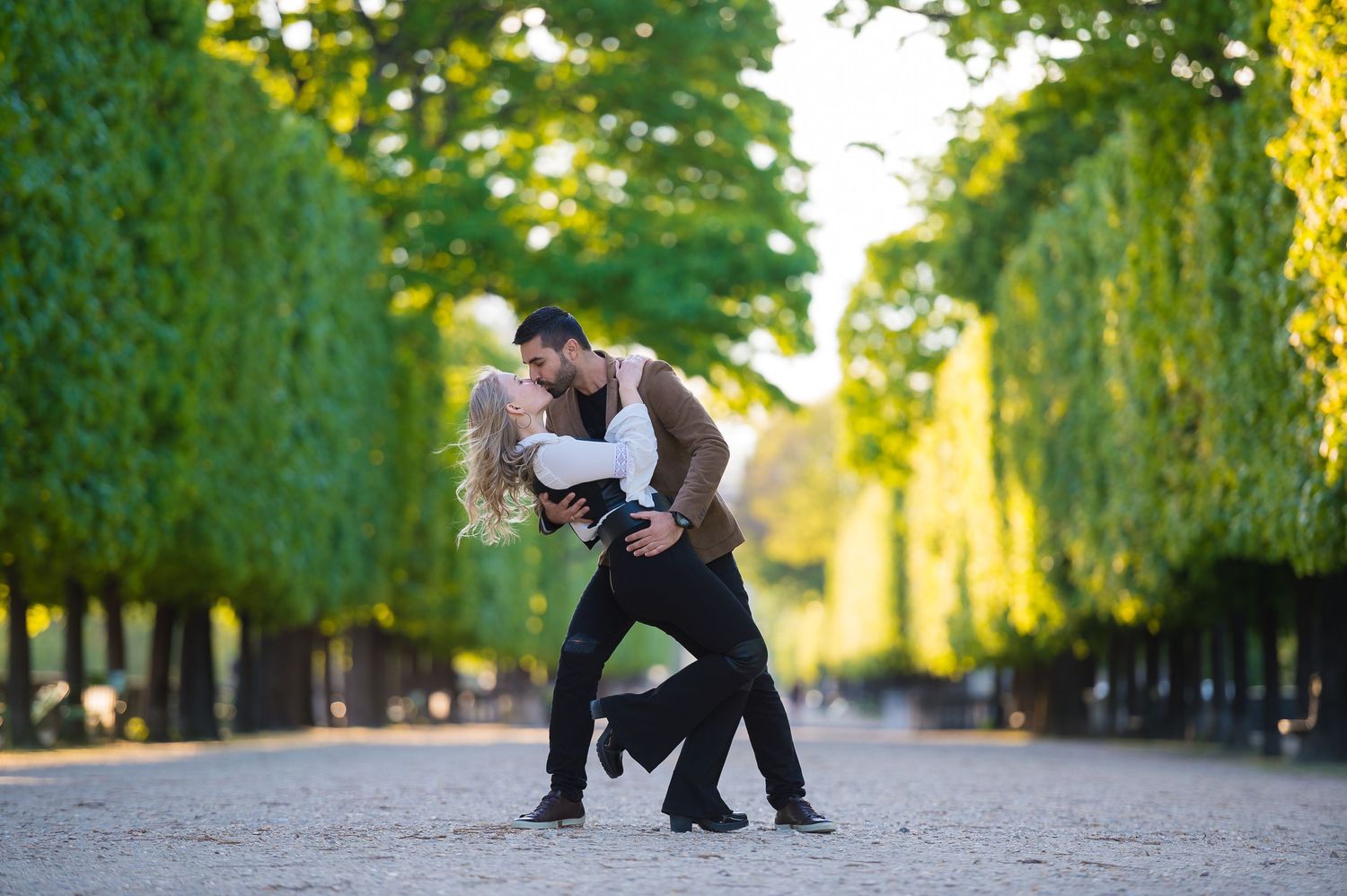 Dancing couple performing a romantic dip move on a tree-lined pathway in Paris.