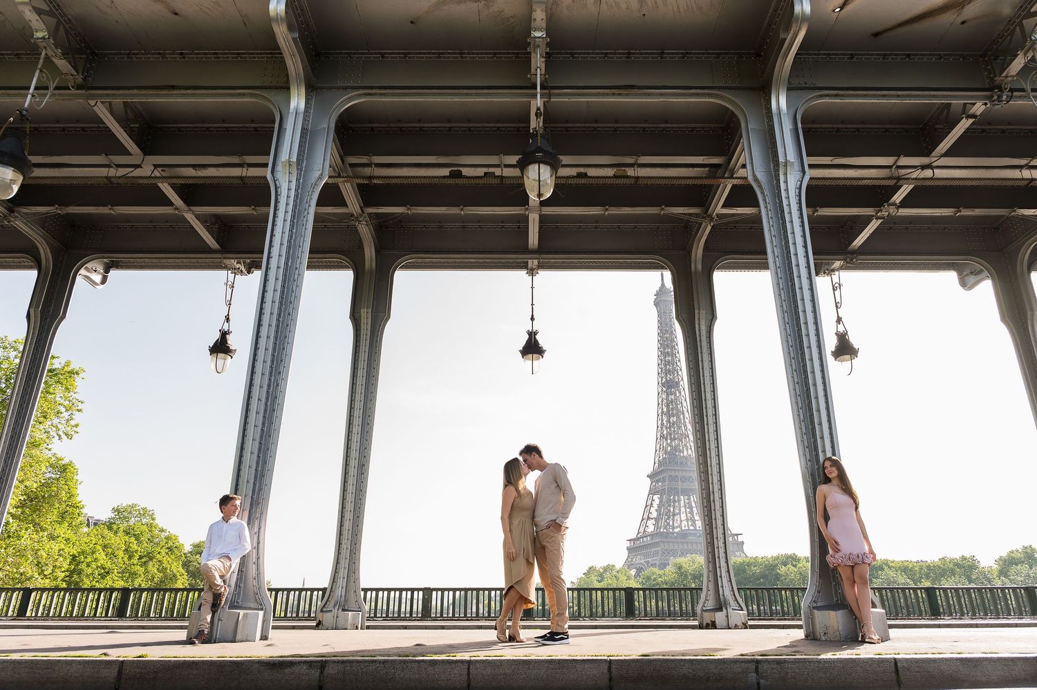 Couple kissing under Bir-Hakeim bridge with Eiffel Tower in background on a sunny Paris day.