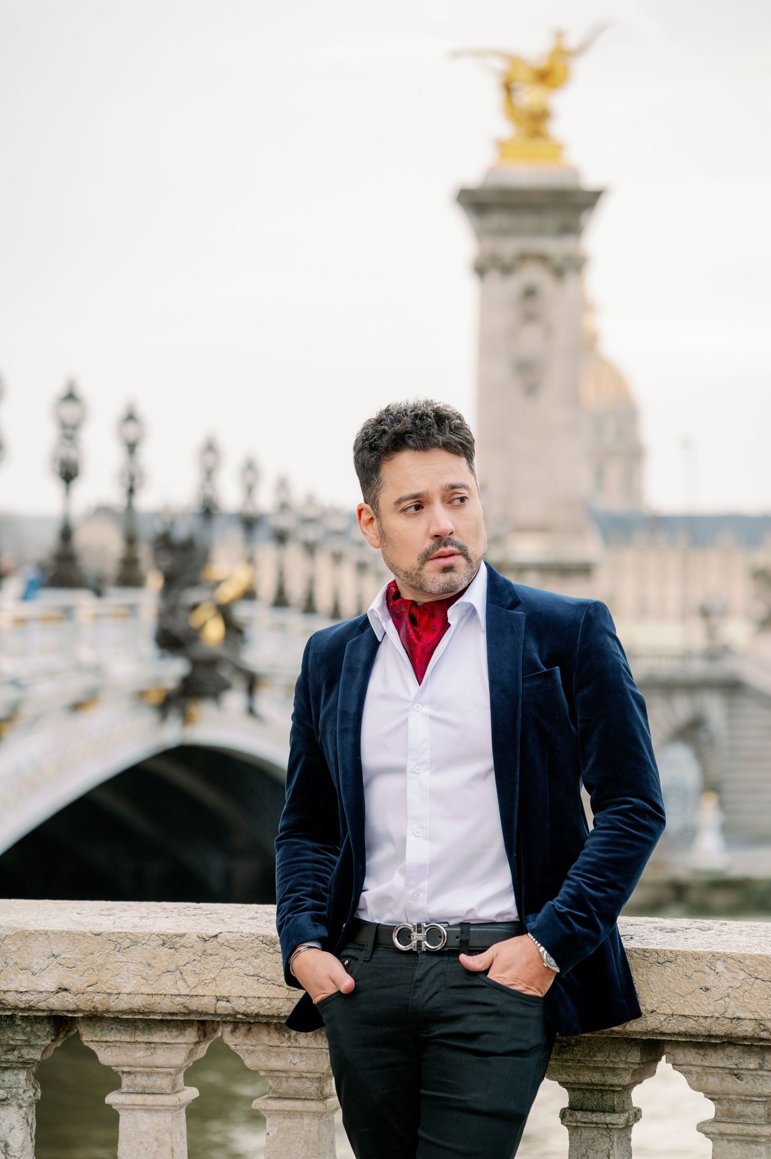 Elegant person in navy velvet blazer and white shirt posing near ornate bridge with golden statues in Paris.