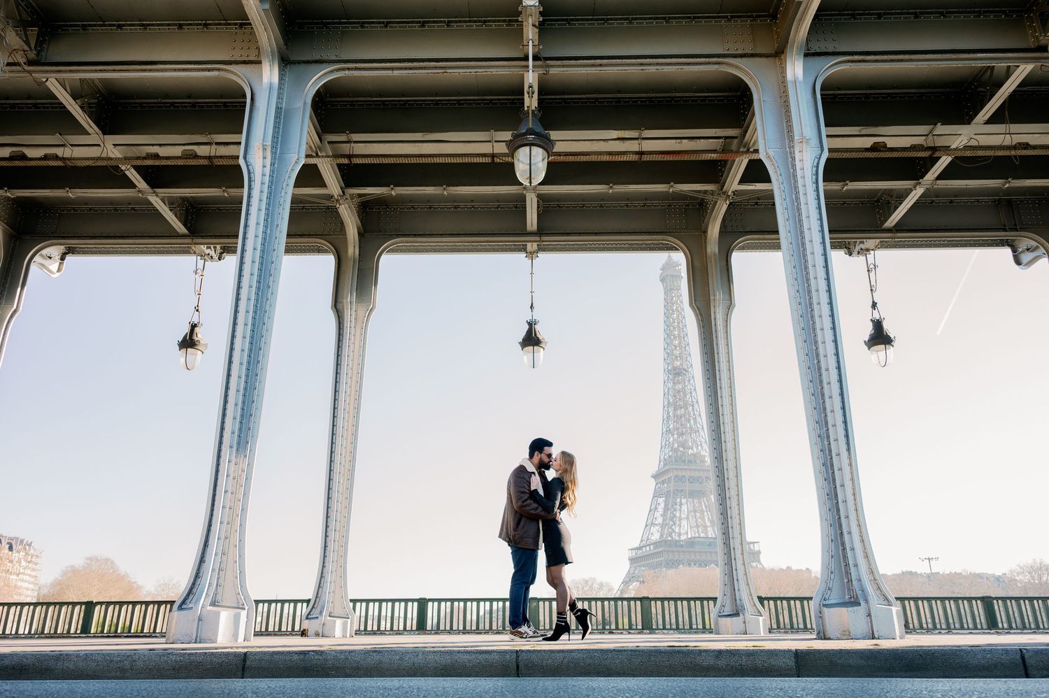 A silhouetted couple shares an intimate moment under a bridge with the Eiffel Tower visible in the distance.