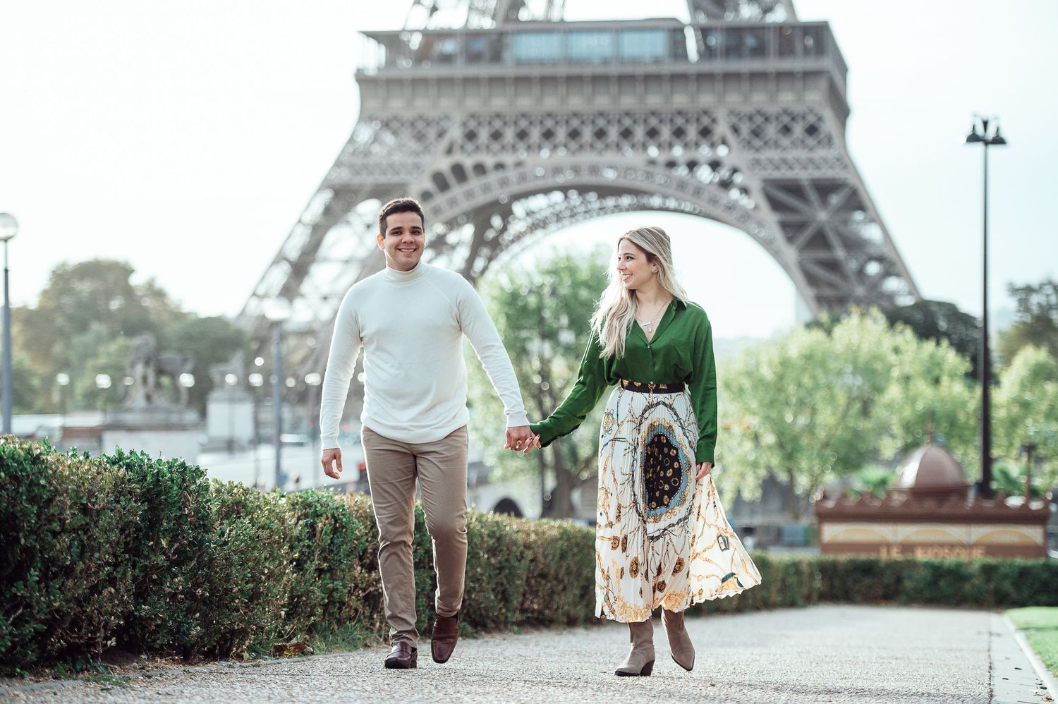 A couple takes a romantic stroll together along a path near the iconic Eiffel Tower in Paris.