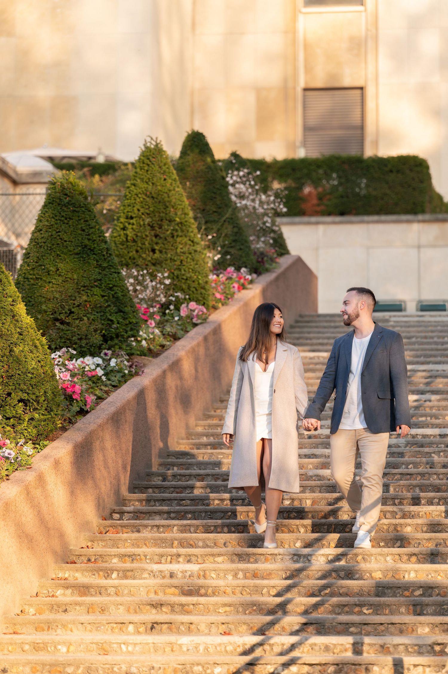 A couple shares romantic moments on stone steps surrounded by manicured gardens and bushes at sunset.