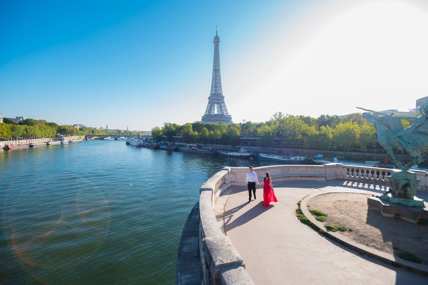 Couple posing near the Seine River with the Eiffel Tower in the background on a sunny day in Paris.