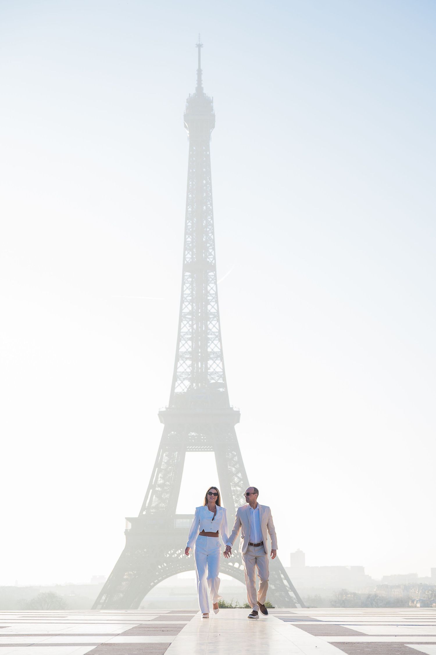 A couple strolling on the Trocadero plaza with the Eiffel Tower rising majestically in the morning haze.