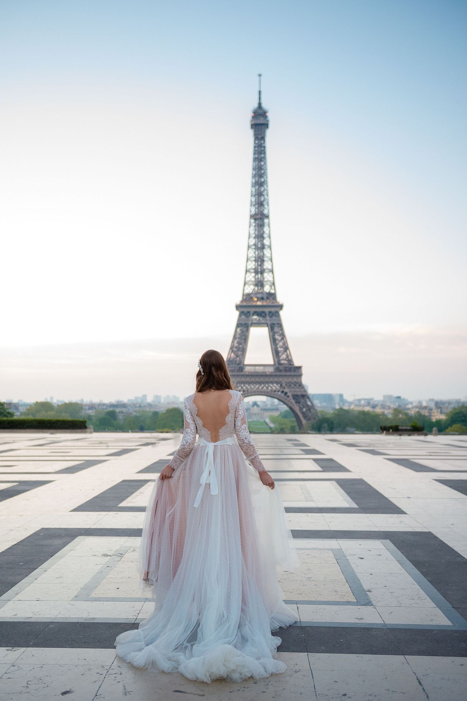 Bride in flowing white gown poses in front of Eiffel Tower during golden hour.