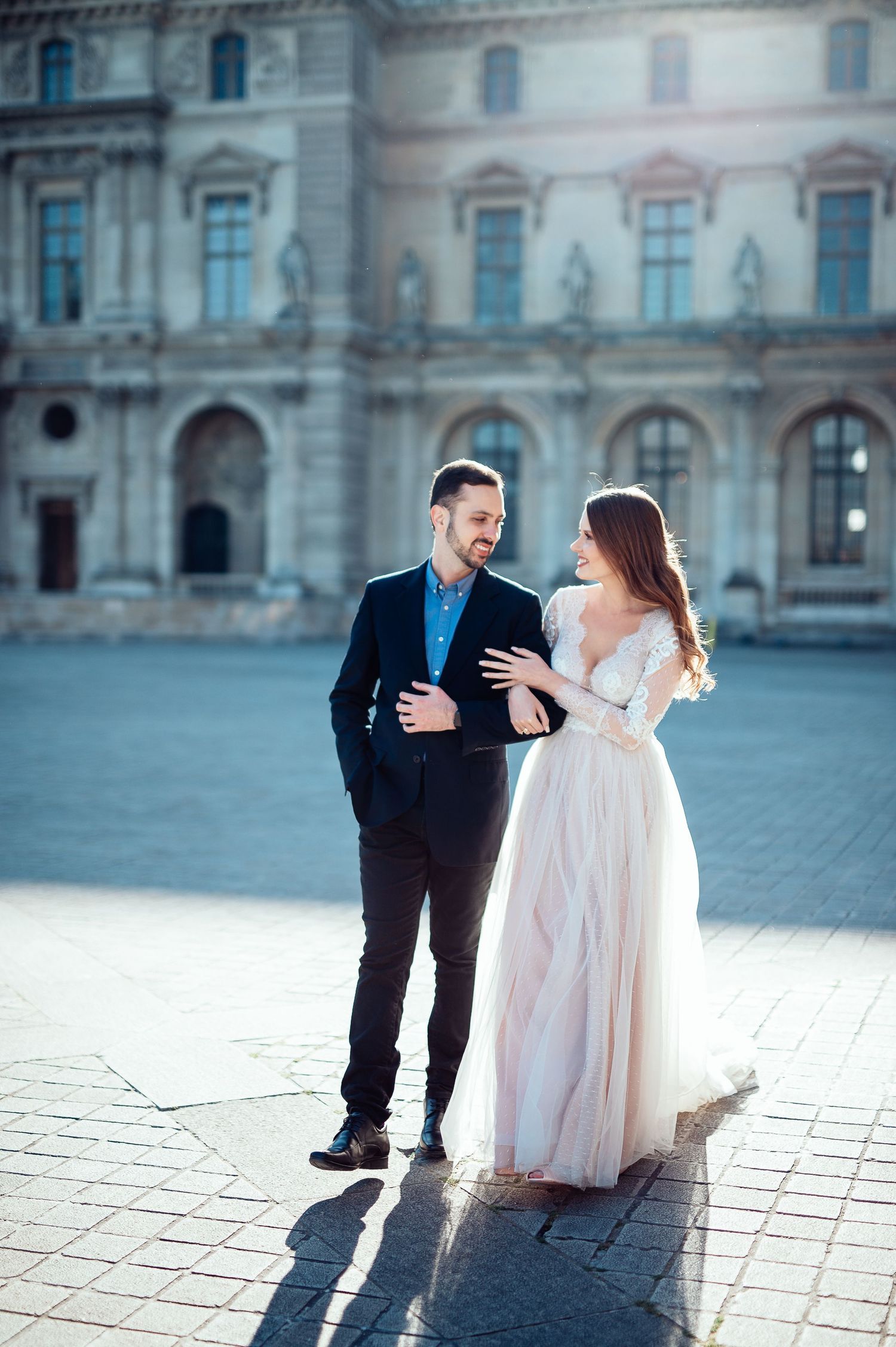 Elegantly dressed couple sharing intimate moment in front of historic Parisian architecture.