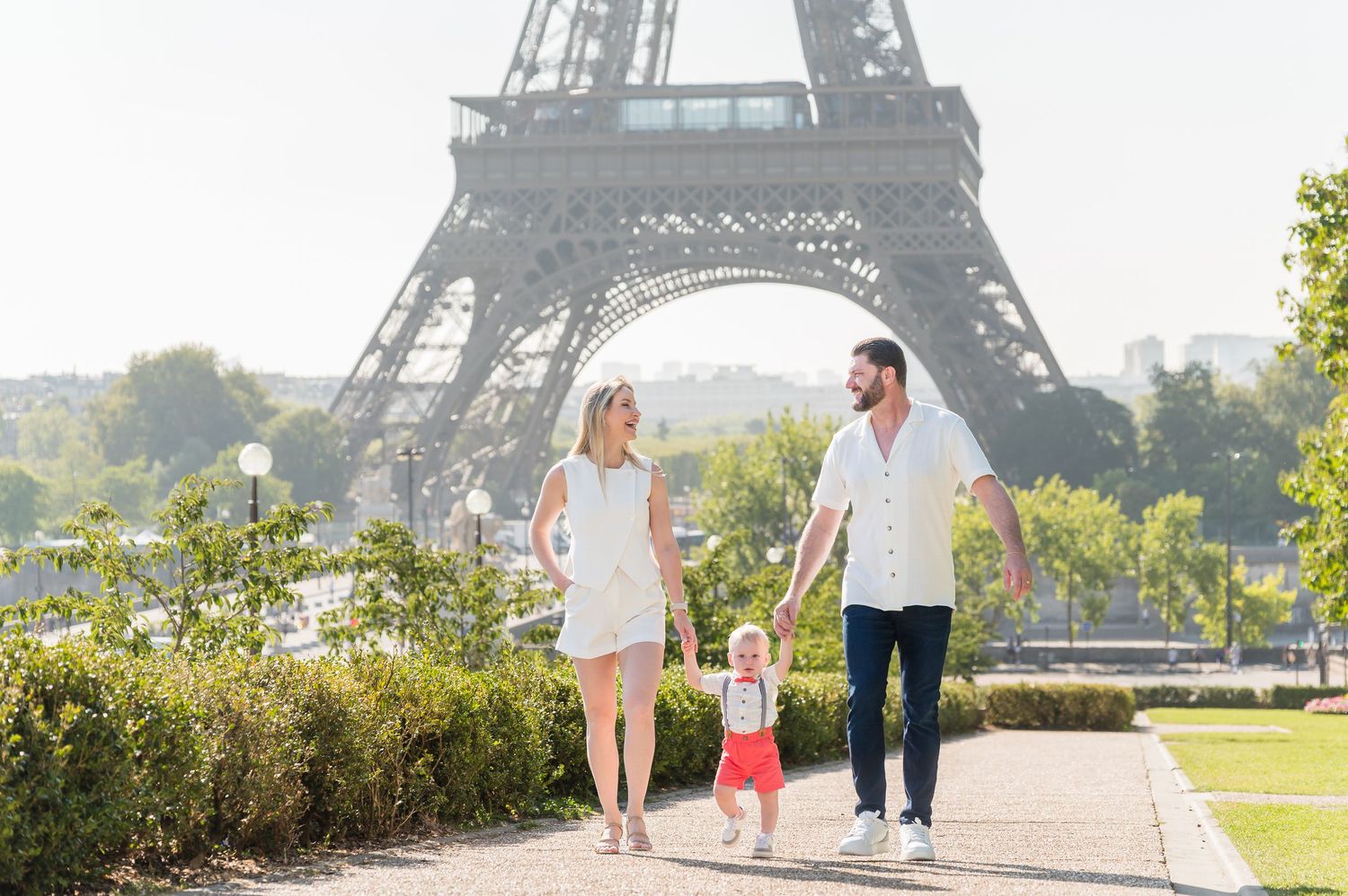 Family walking on pathway near the Eiffel Tower in Paris during a sunny day with iconic landmark in background.