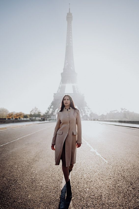 A lone figure in a beige coat stands on an empty road with the iconic Eiffel Tower rising in the misty background.