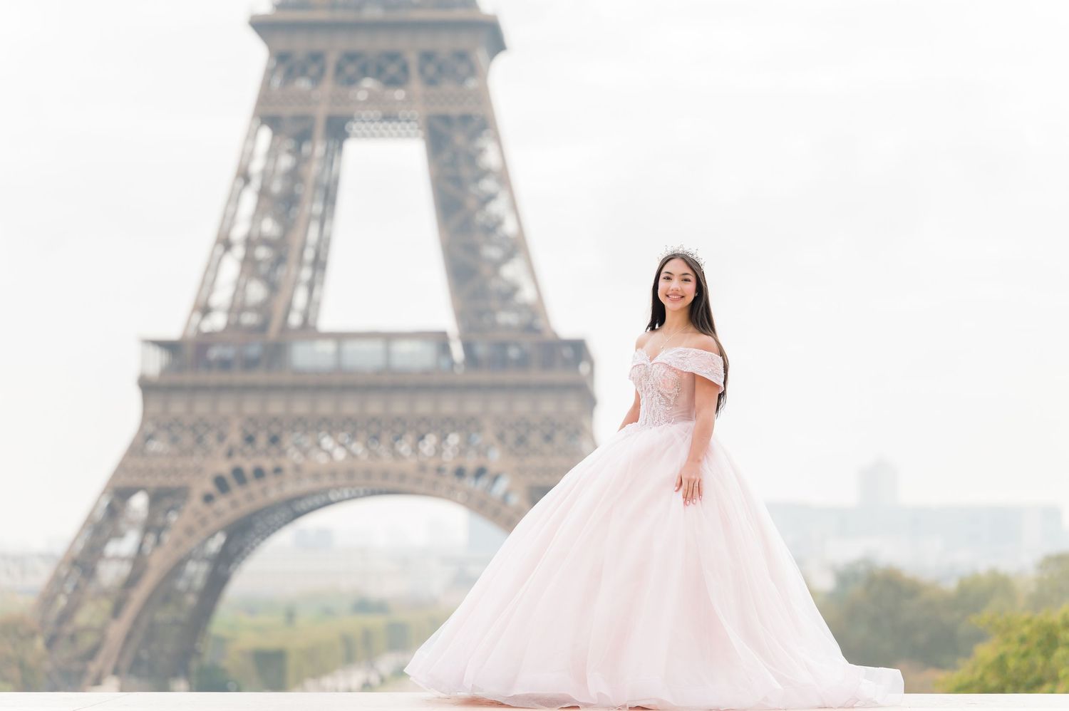 Someone in a flowing pink gown poses for photos in front of the iconic Eiffel Tower in Paris.