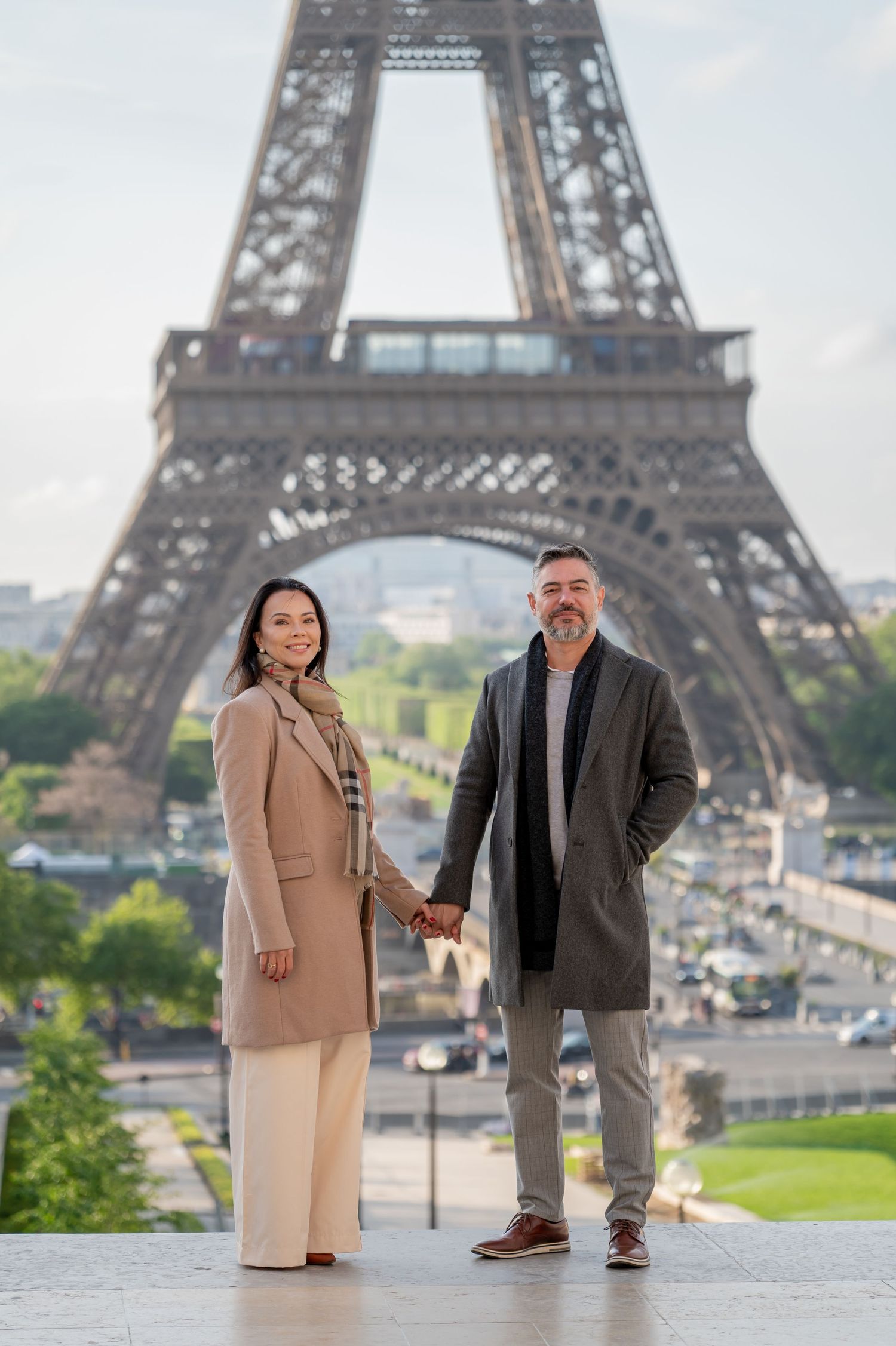 Couple in elegant coats posing together with Eiffel Tower in background.
