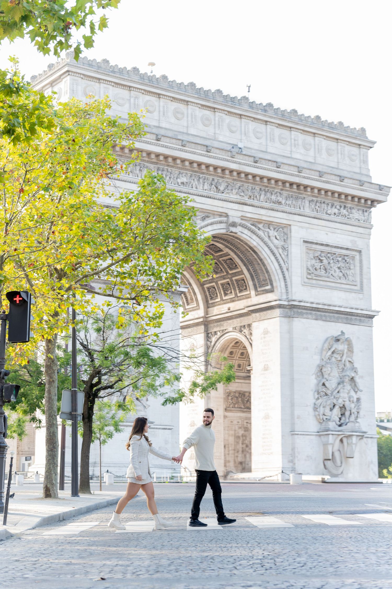 Couple holding hands walking in front of the Arc de Triomphe in Paris on a sunny day.