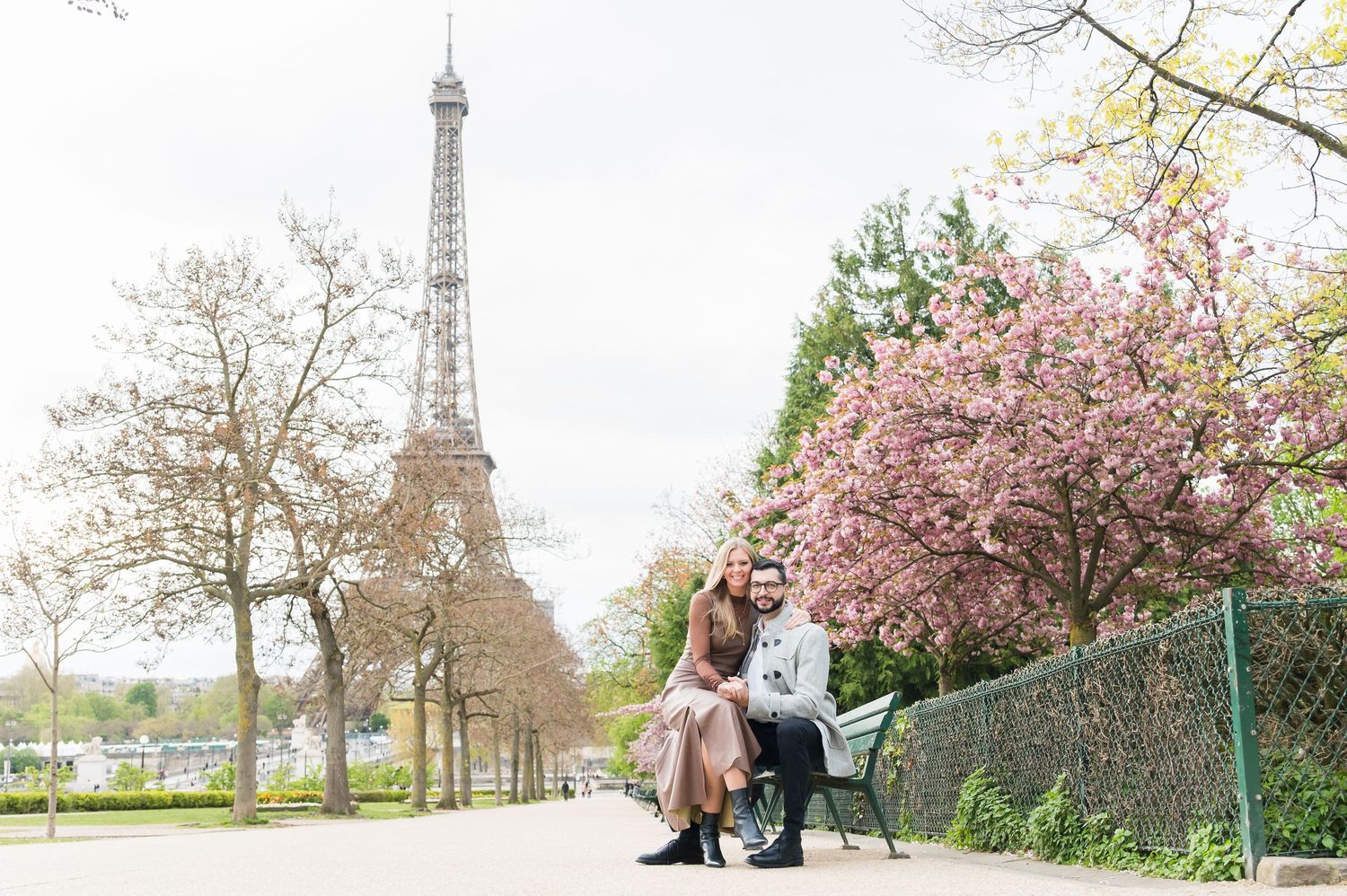 Couple sitting on a bench near the Eiffel Tower in Paris with cherry blossoms blooming in spring.
