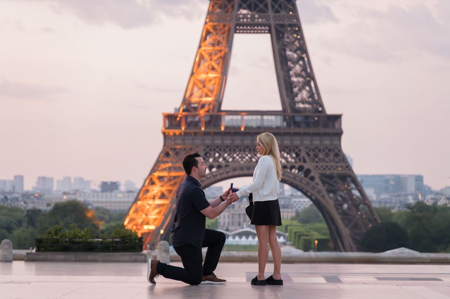 Romantic marriage proposal silhouettes in front of illuminated Eiffel Tower at sunset in Paris, France.