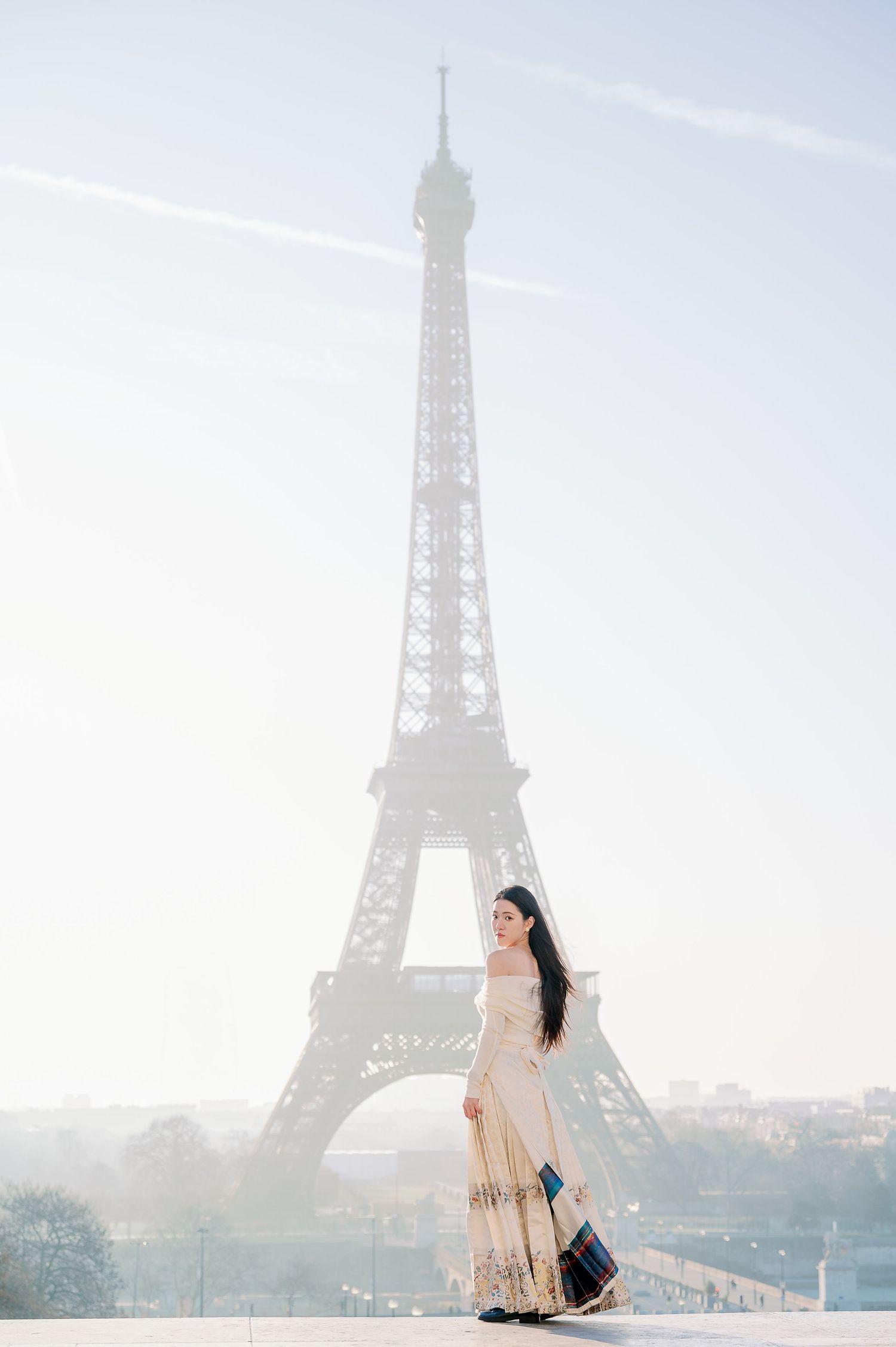 A graceful figure in an embellished dress poses against the iconic Eiffel Tower backdrop.