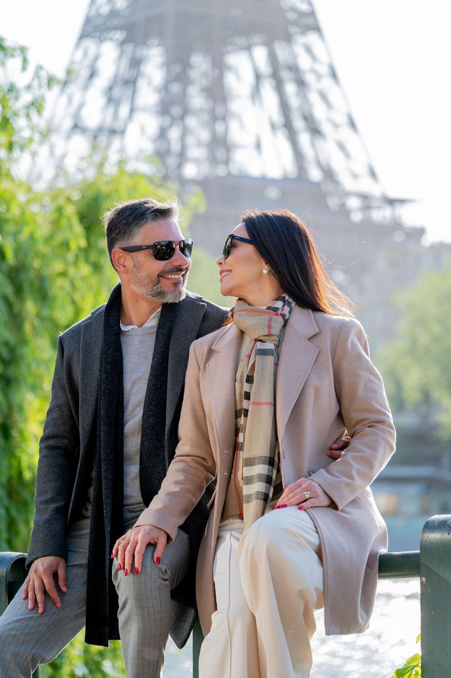 Fashionable couple in coats sharing intimate moment near Eiffel Tower on spring day.