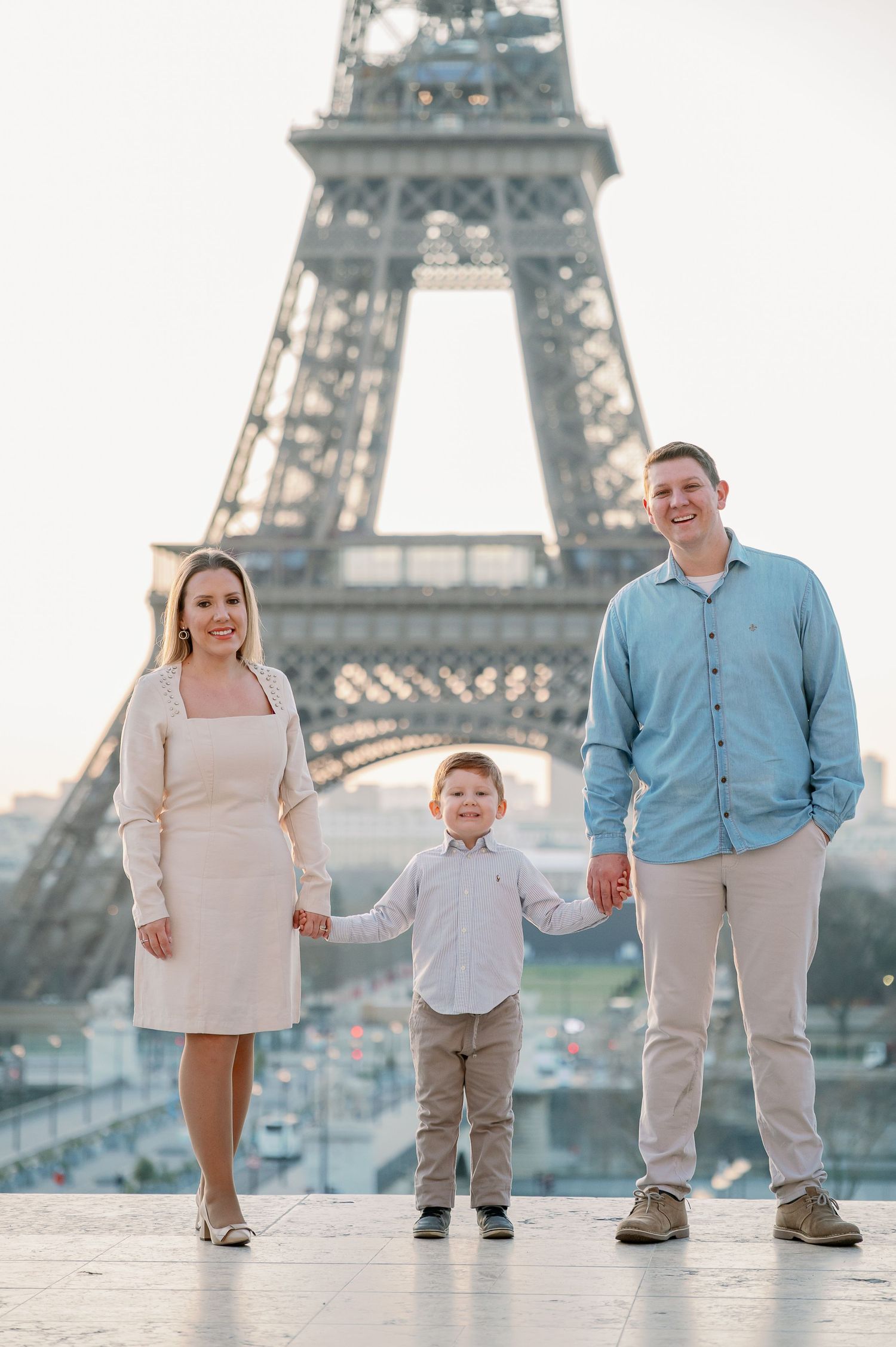Family of three poses together in front of iconic Eiffel Tower at sunset.