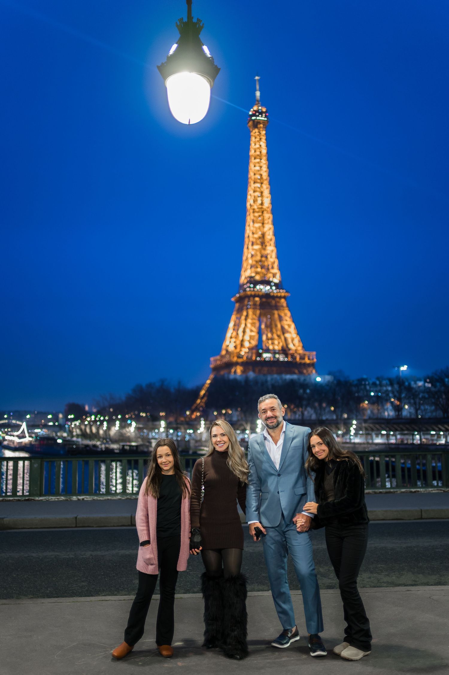 Family of four posing in front of the illuminated Eiffel Tower at night in Paris, France.