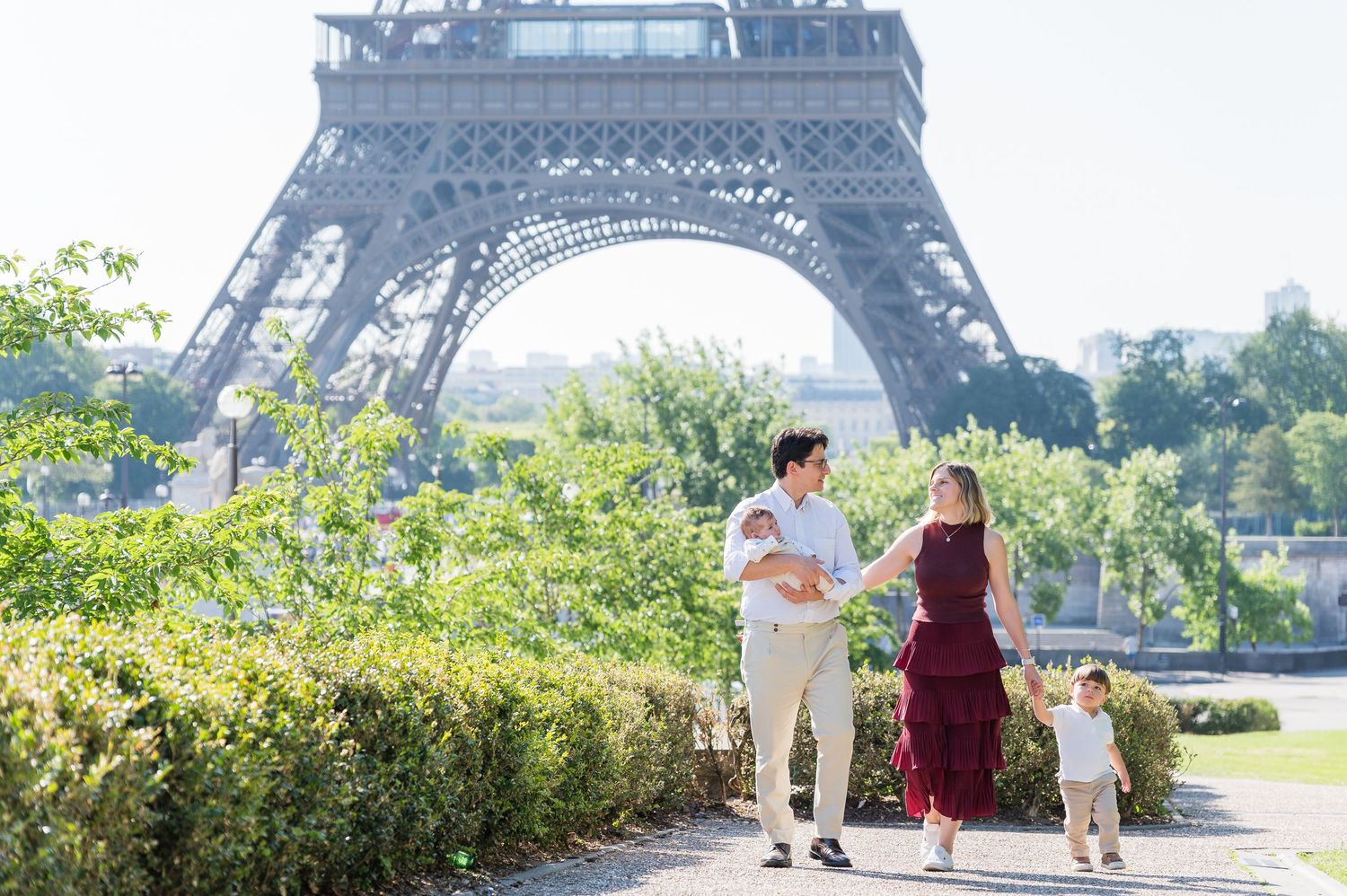 A young family strolls in a garden near the Eiffel Tower in Paris on a sunny summer day.