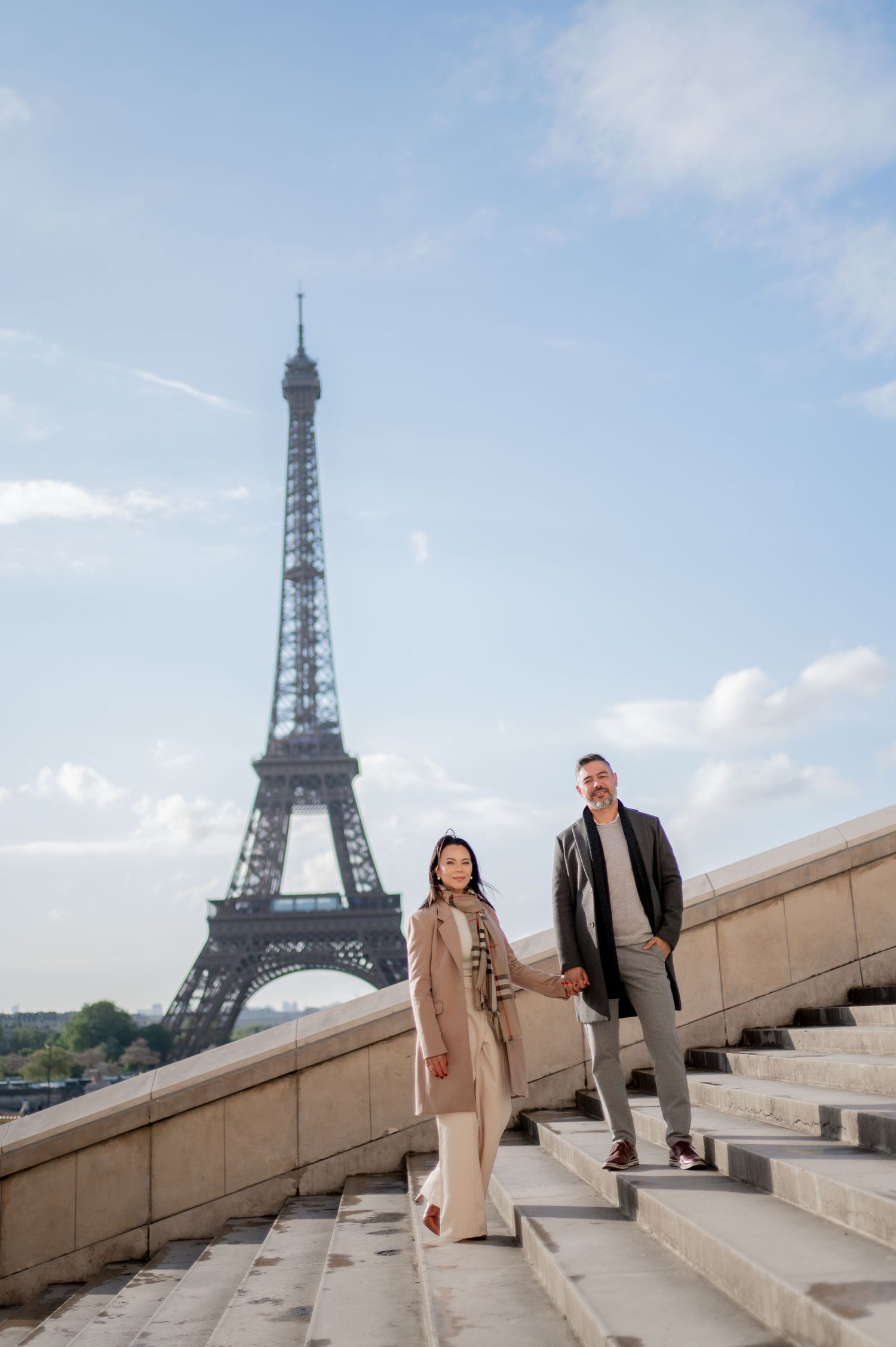 Stylish pair posing on stone steps with iconic Eiffel Tower framed behind them in Paris.