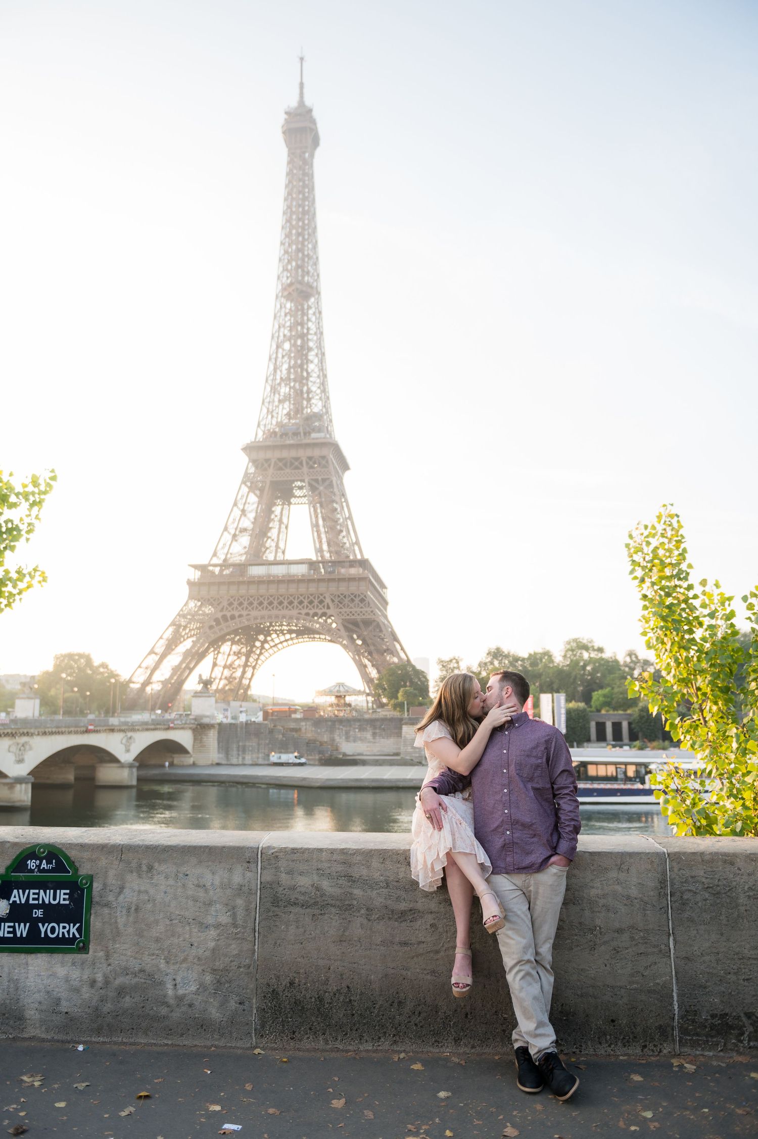 Couple shares romantic moment by Seine River wall with Eiffel Tower and sunset in background.