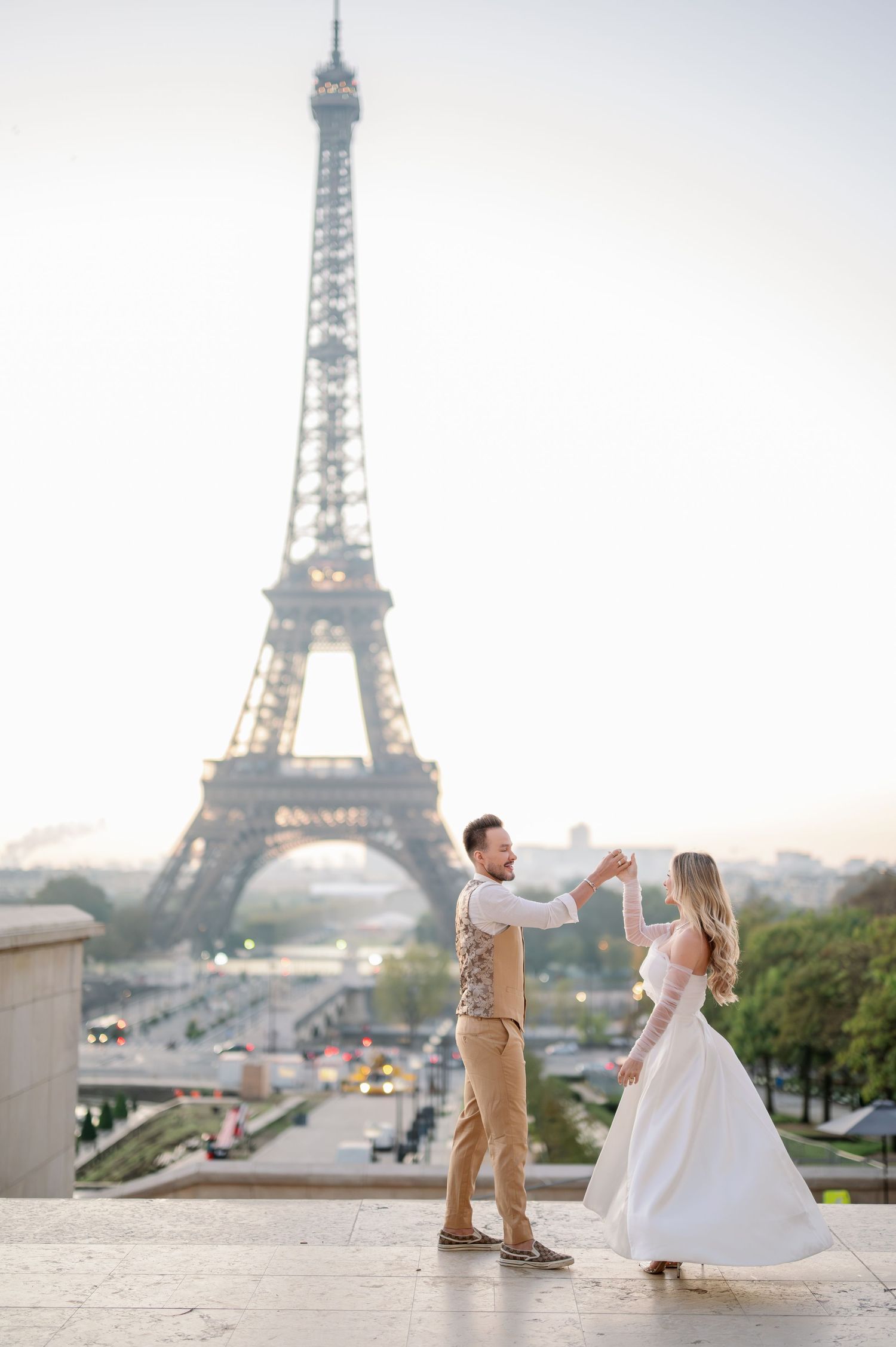A couple dances together at Trocadero with the iconic Eiffel Tower visible in the misty Paris background.