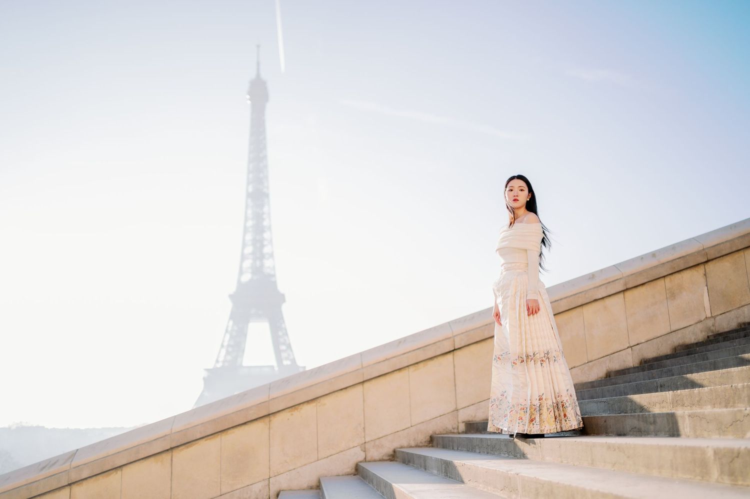 A feminine silhouette in a flowing dress poses on Trocadero steps with the Eiffel Tower behind.